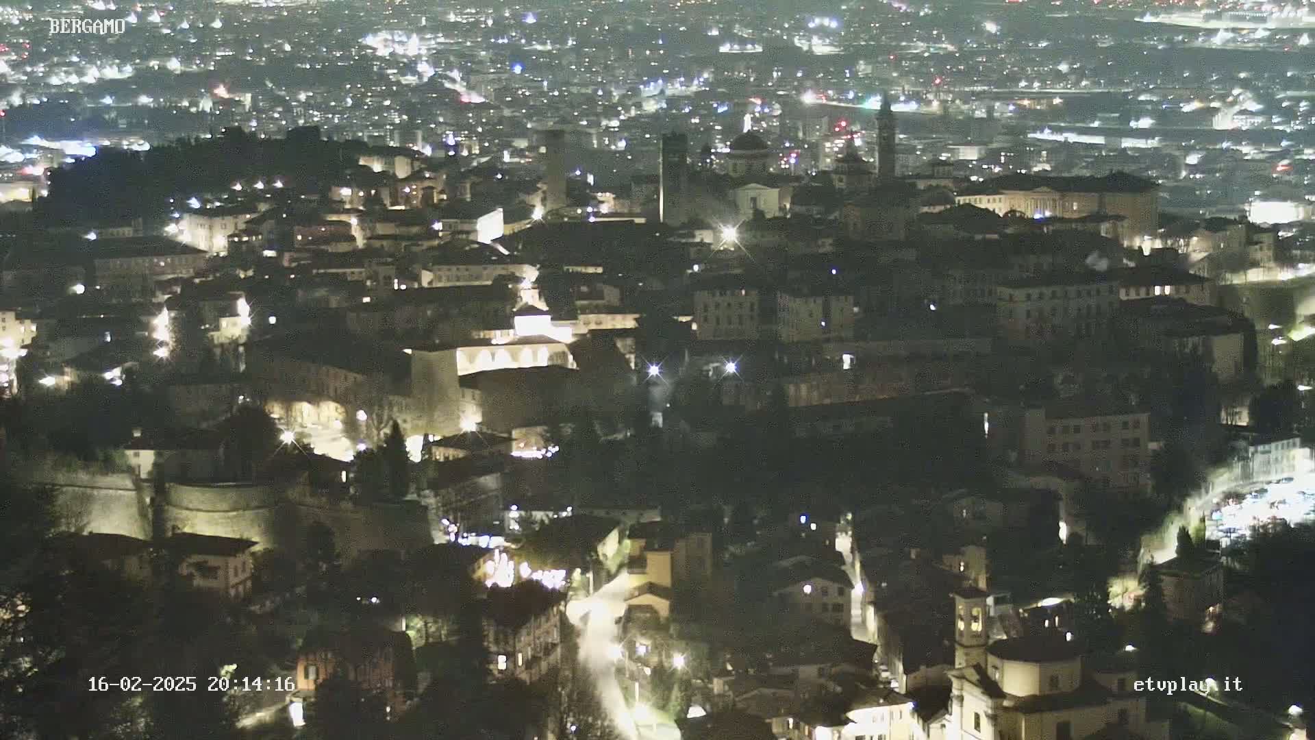 A nighttime aerial view of a city, showing numerous illuminated buildings and streets.