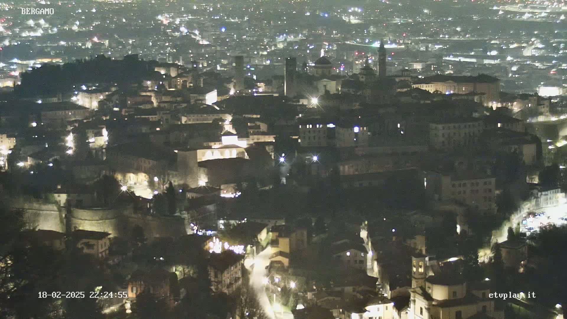 A nighttime aerial view of a city, showing a densely packed collection of buildings illuminated by lights.