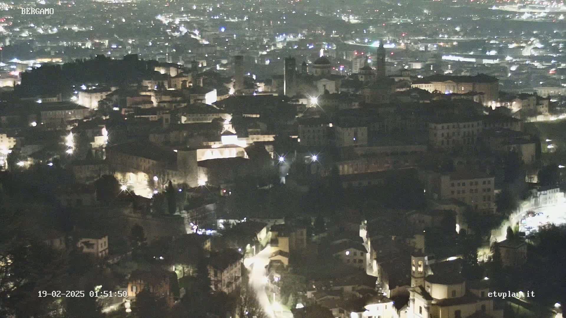 A nighttime, aerial view of a city with many illuminated buildings and streets.