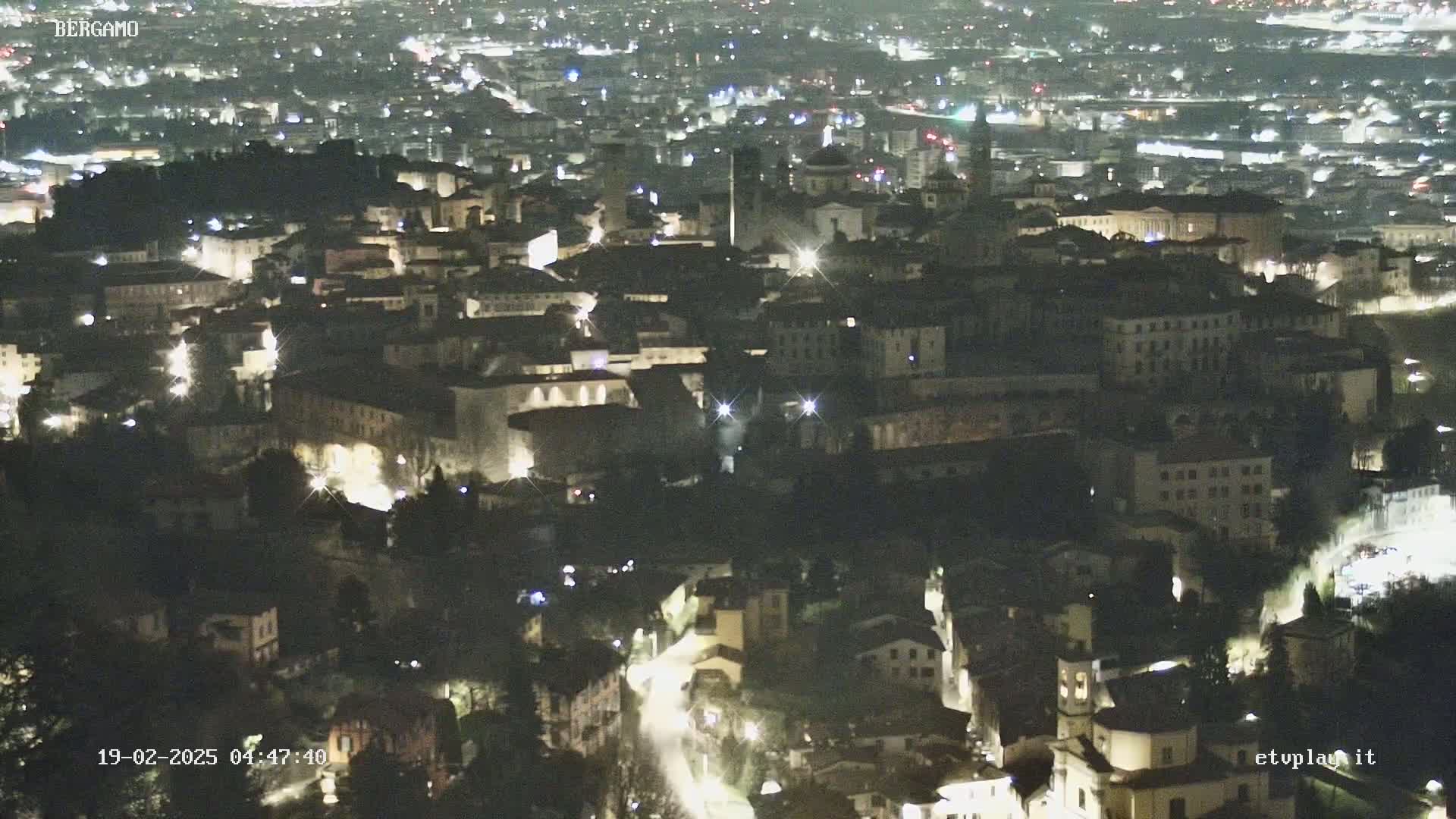 A nighttime aerial view of a city with buildings illuminated by streetlights.