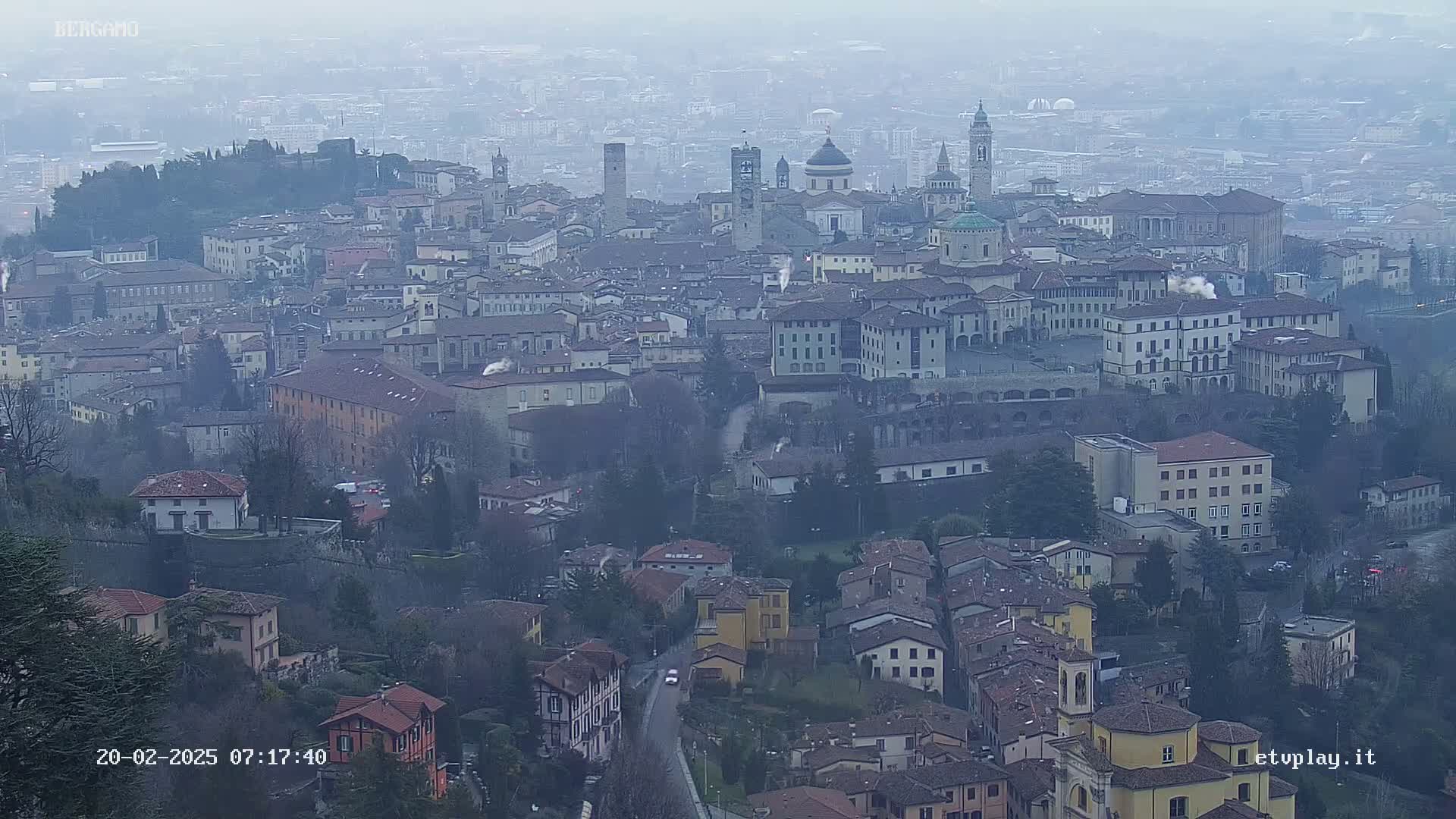 A hazy view of a city with many buildings of varying heights and architectural styles, seen from a high vantage point on a cloudy day.