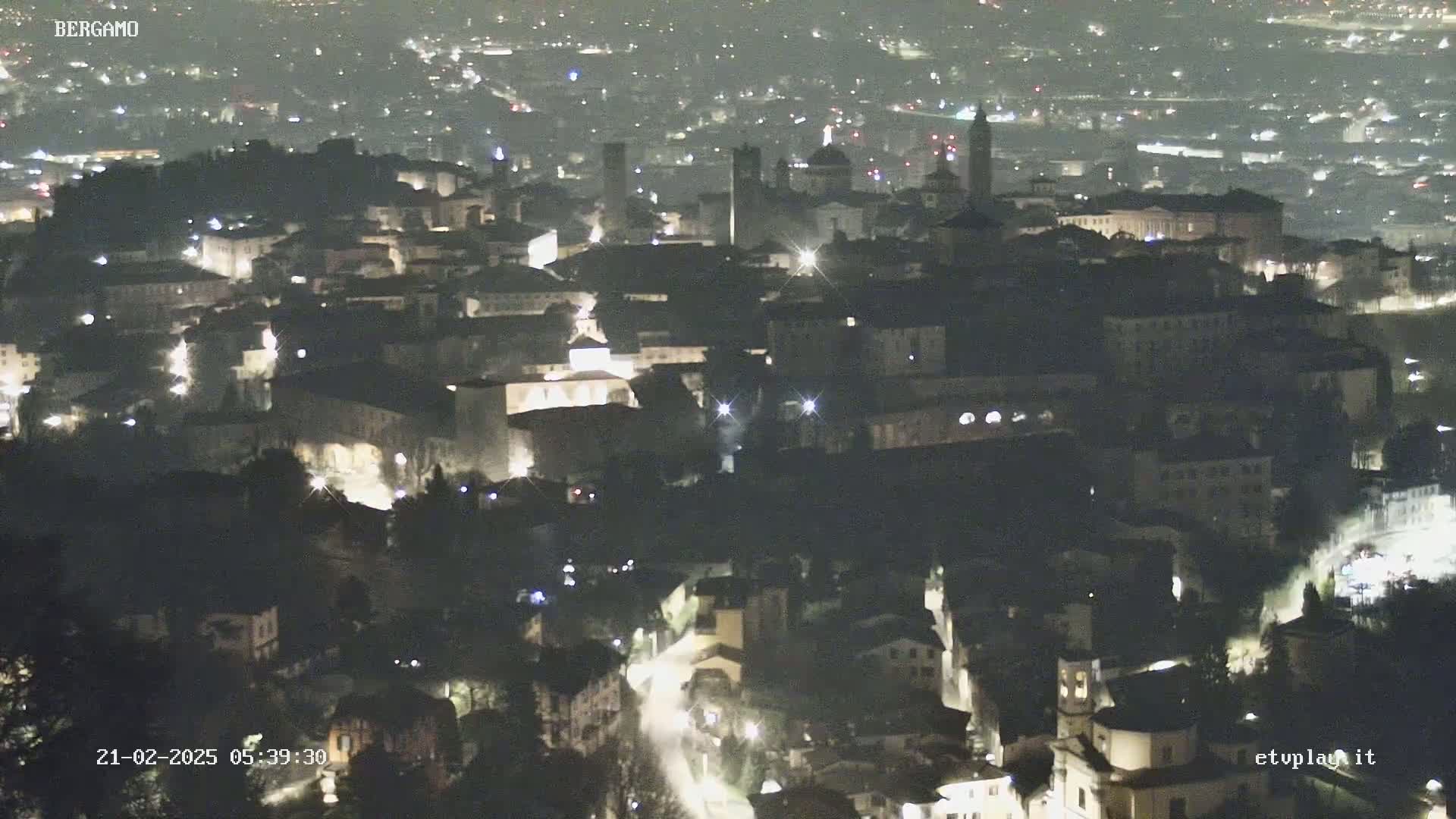 A nighttime aerial view of a city with dimly lit buildings and streets, under a clear sky.