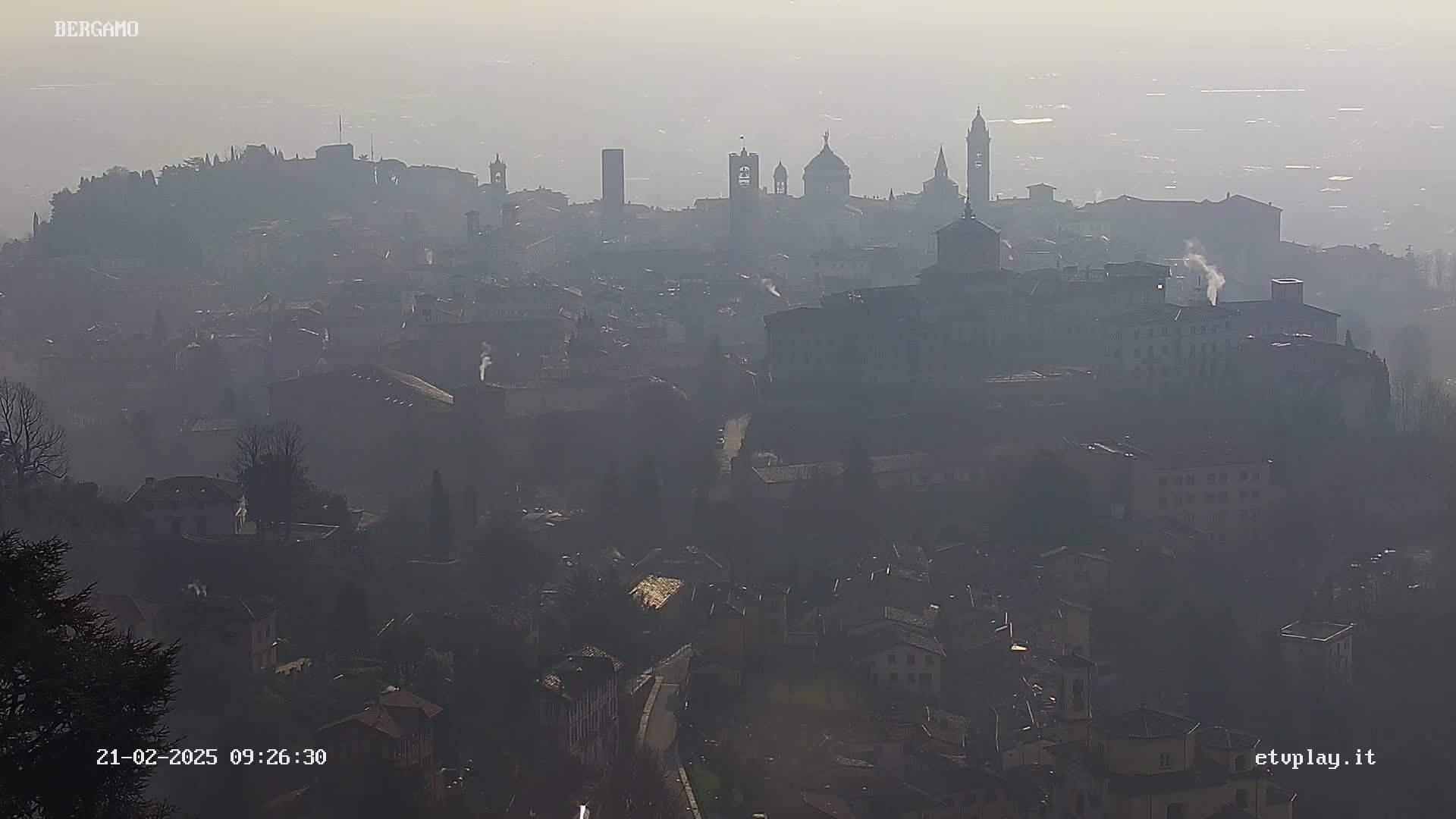 A hazy, distant view of a city with numerous buildings and spires, under a foggy sky.