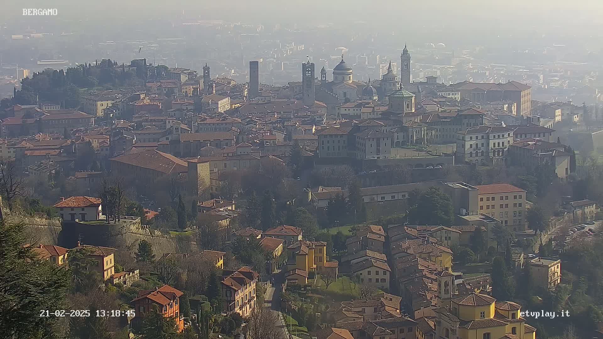 A hazy view of a sprawling city with numerous buildings of varying heights and architectural styles, situated on a hillside.