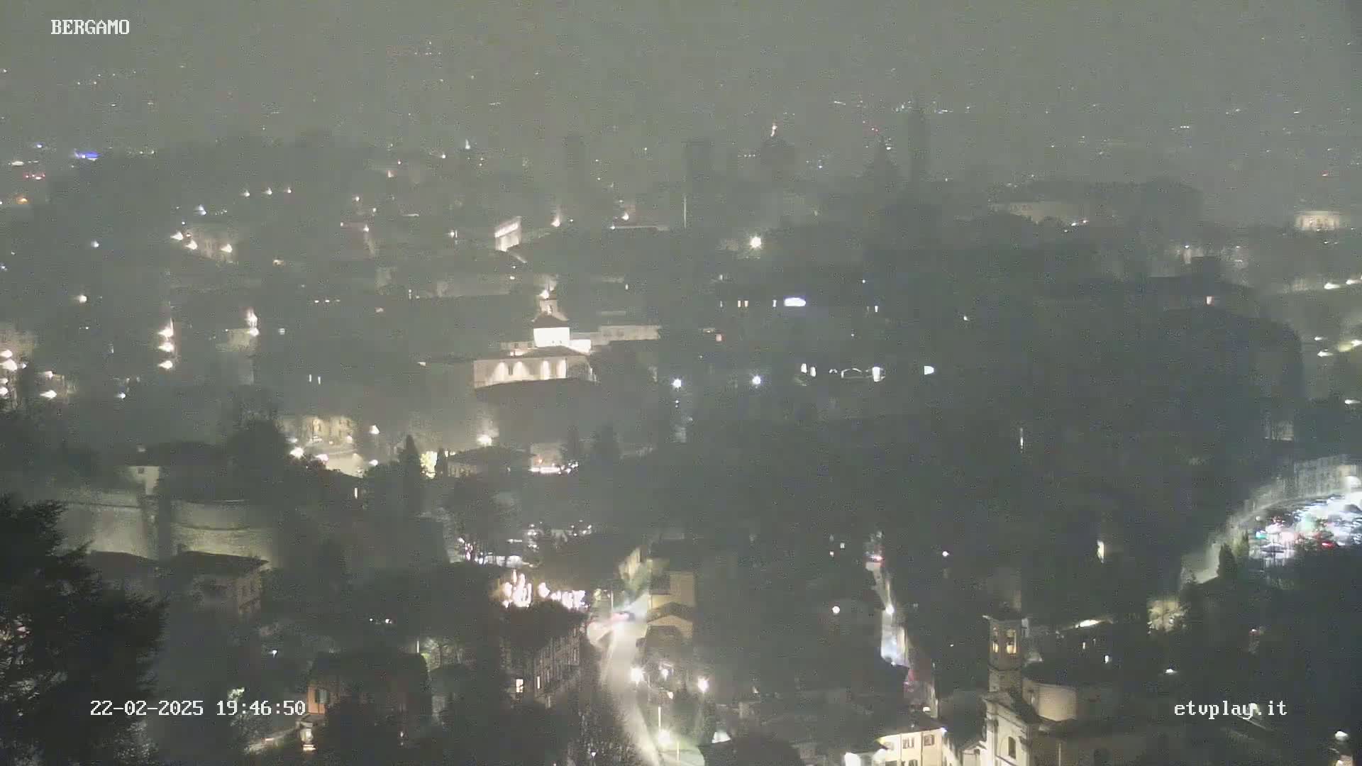 A nighttime, hazy view of a city with dimly lit buildings and streets.