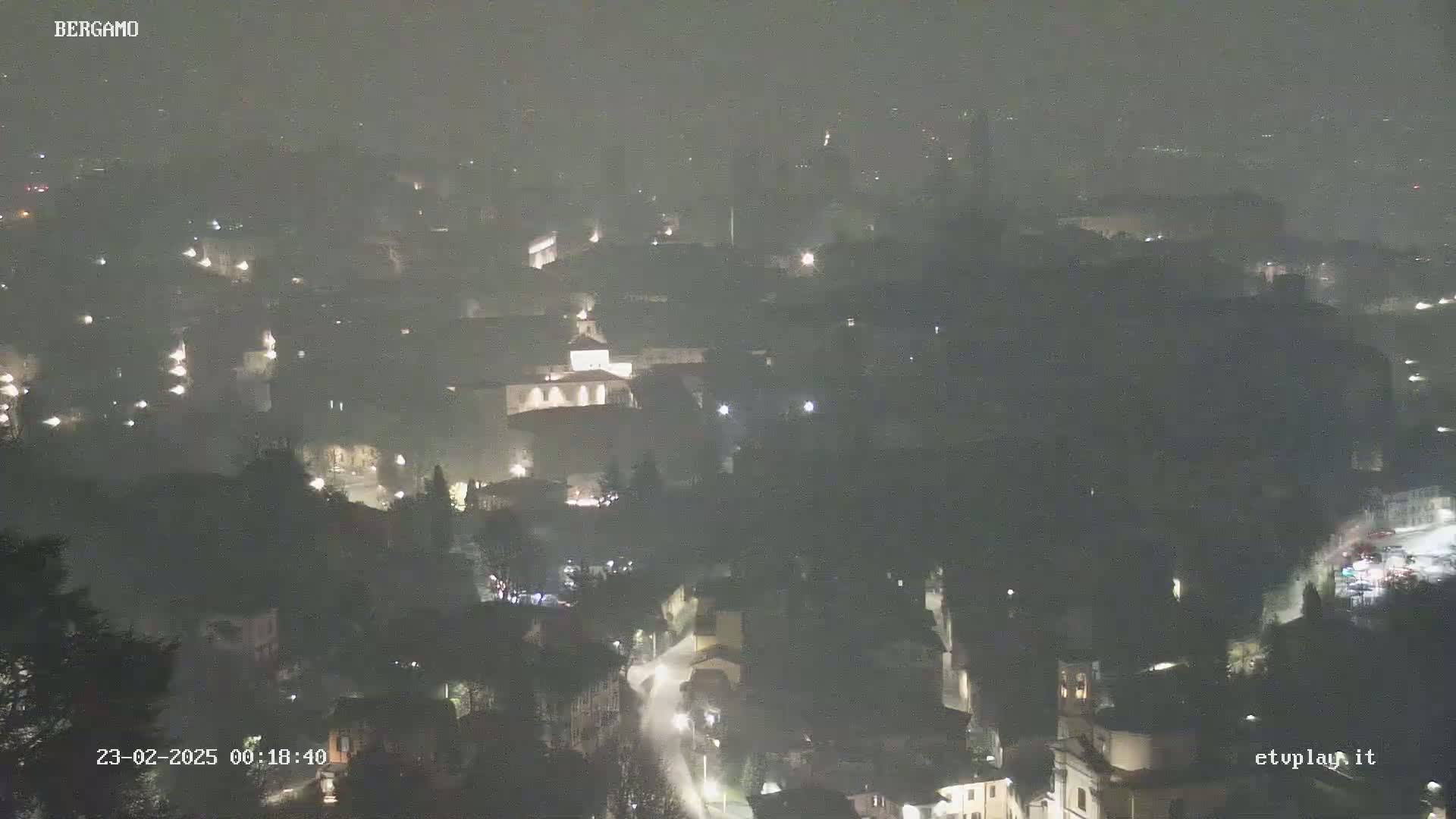 A nighttime, hazy view of a city with sparsely lit buildings and roads.