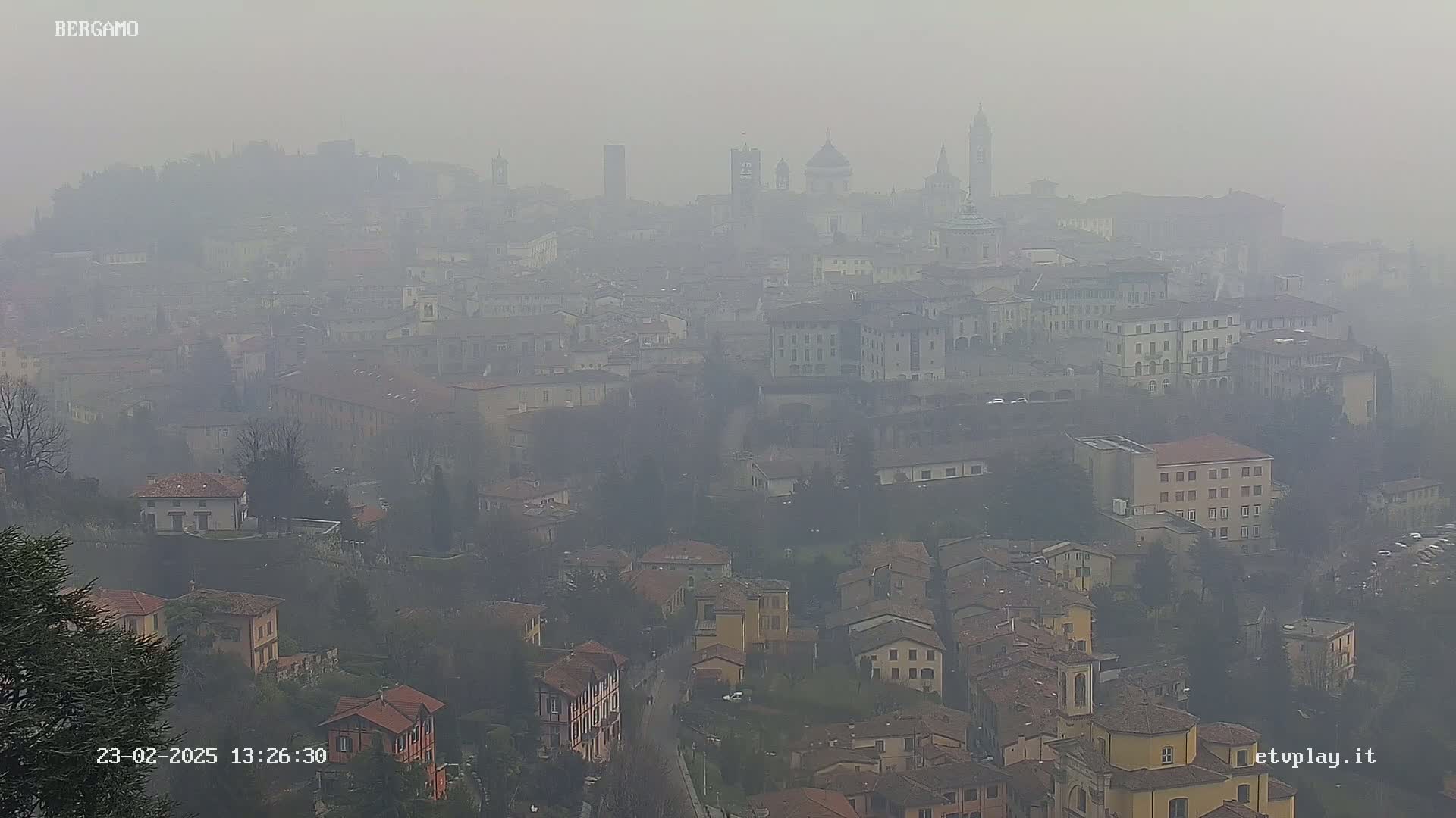 A hazy, distant view of a city with numerous buildings, including several prominent structures that appear to be churches or towers, under a foggy sky.