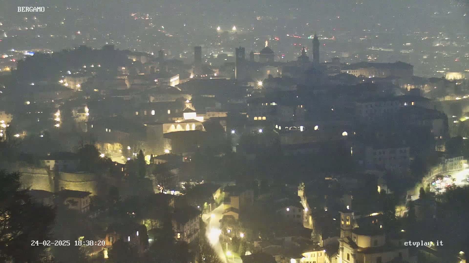 A hazy night view of a city with numerous lights illuminating buildings and streets.