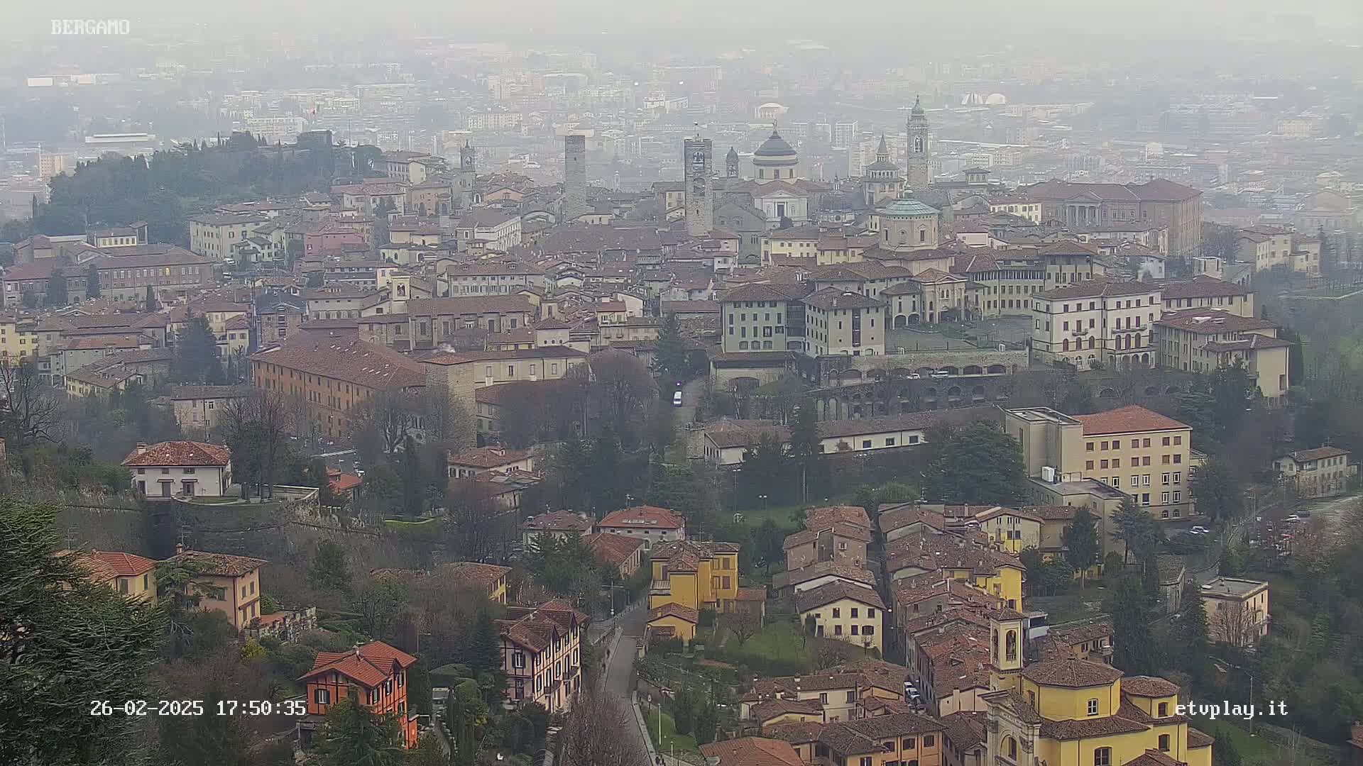 A hazy view of a city with many buildings of varying heights and architectural styles, nestled amongst green hills.
