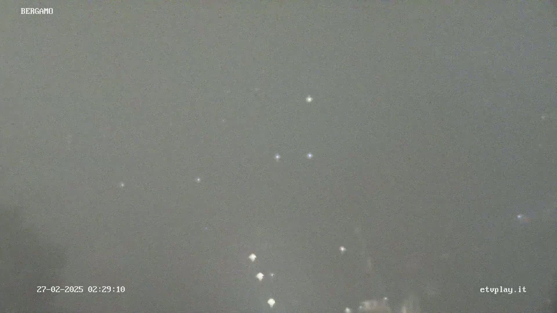 A nighttime, overcast sky shows a few distant lights below and several faint stars above.