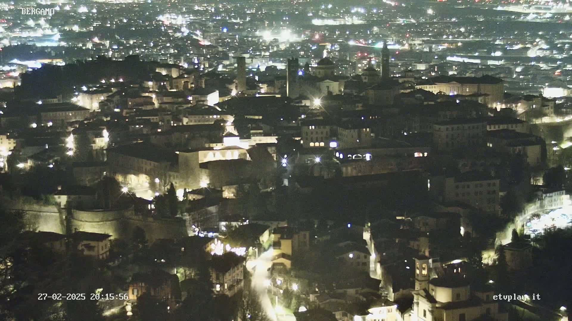 A nighttime, aerial view of a city with many illuminated buildings and streets.