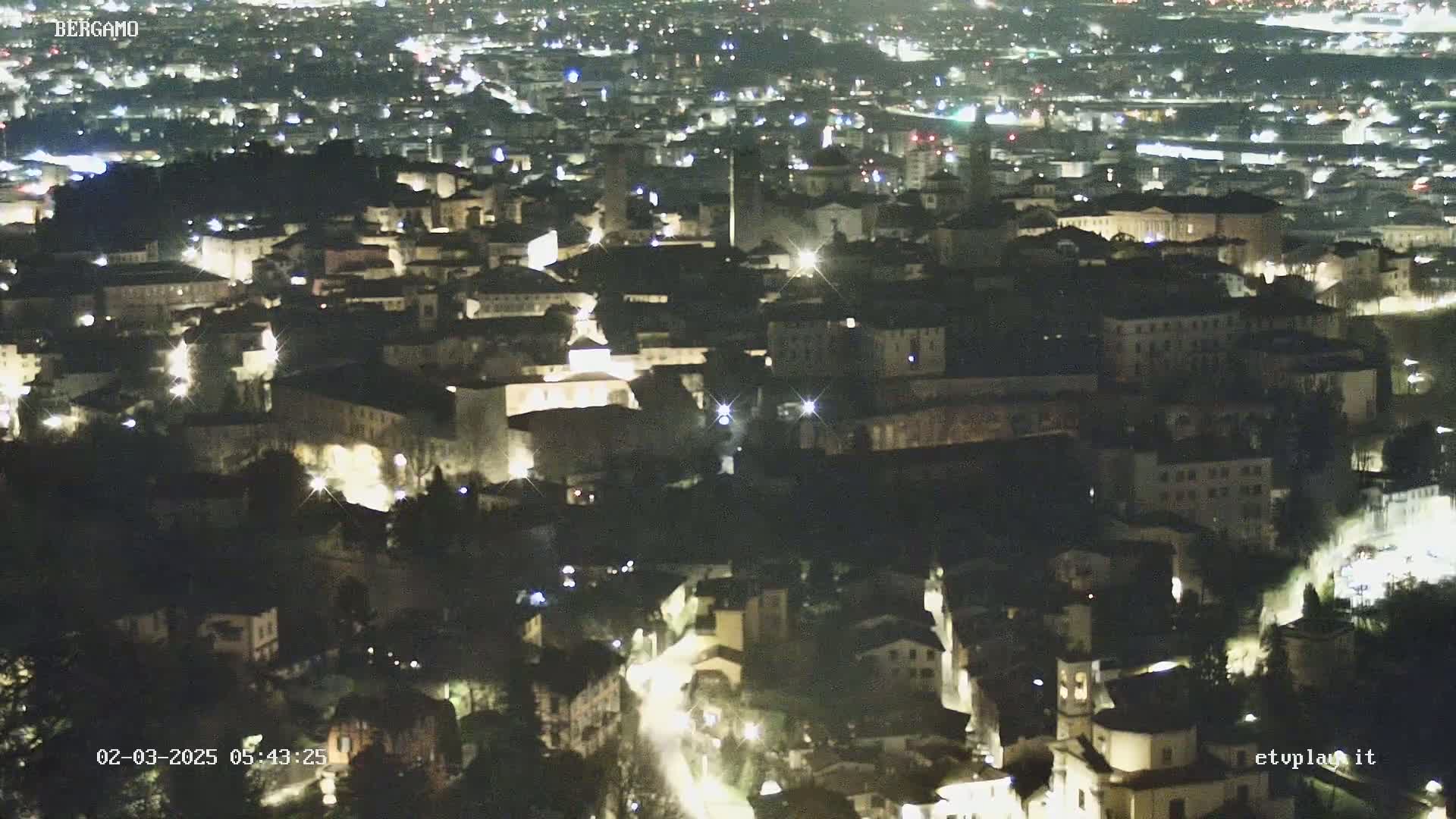 A nighttime, high-angle view of a city illuminated by lights, showing a dense collection of buildings nestled together.