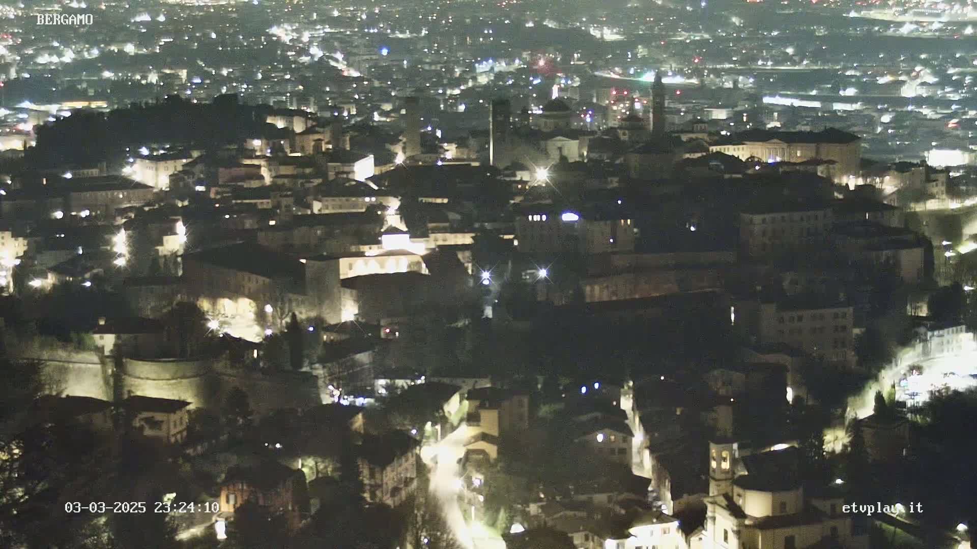 A nighttime aerial view of a city illuminated by lights, showing a dense collection of buildings and streets.