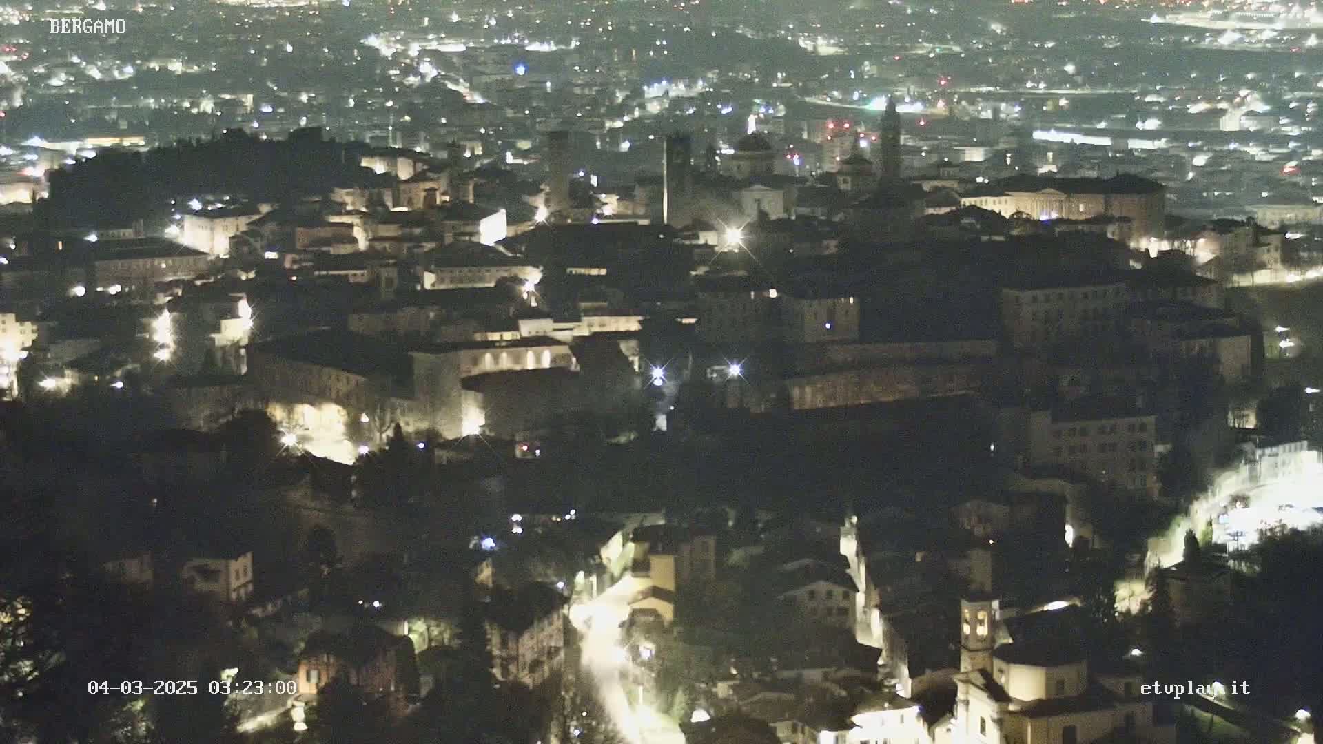 A nighttime, aerial view of a city with numerous illuminated buildings and streets.