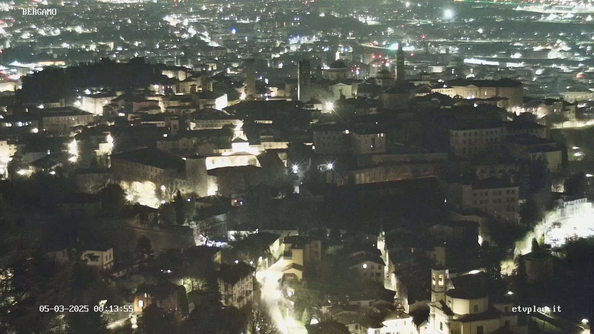 A nighttime, aerial view of a city with many buildings illuminated by streetlights.