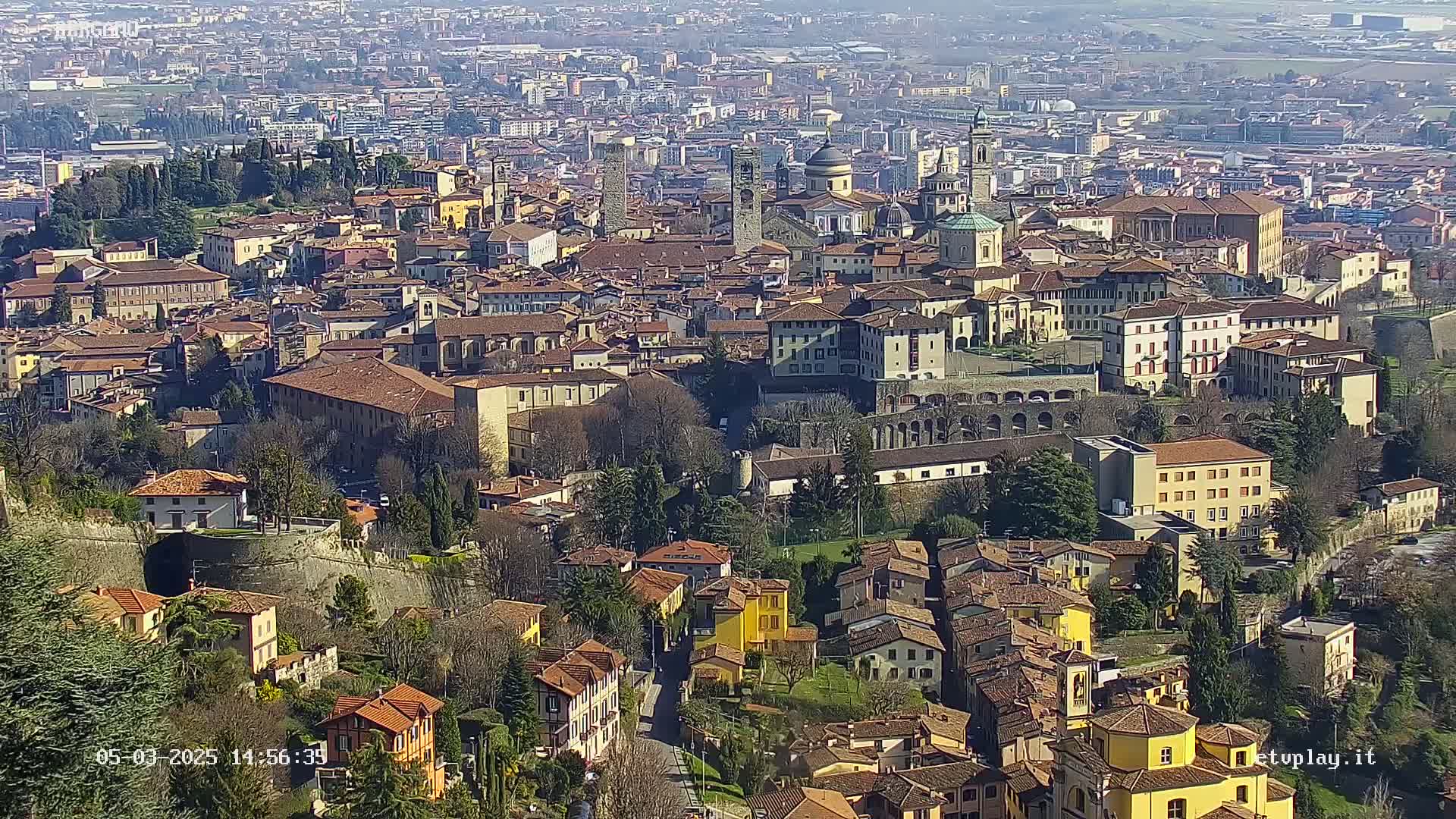 A sprawling city of terracotta-roofed buildings sits under a clear, sunny sky.