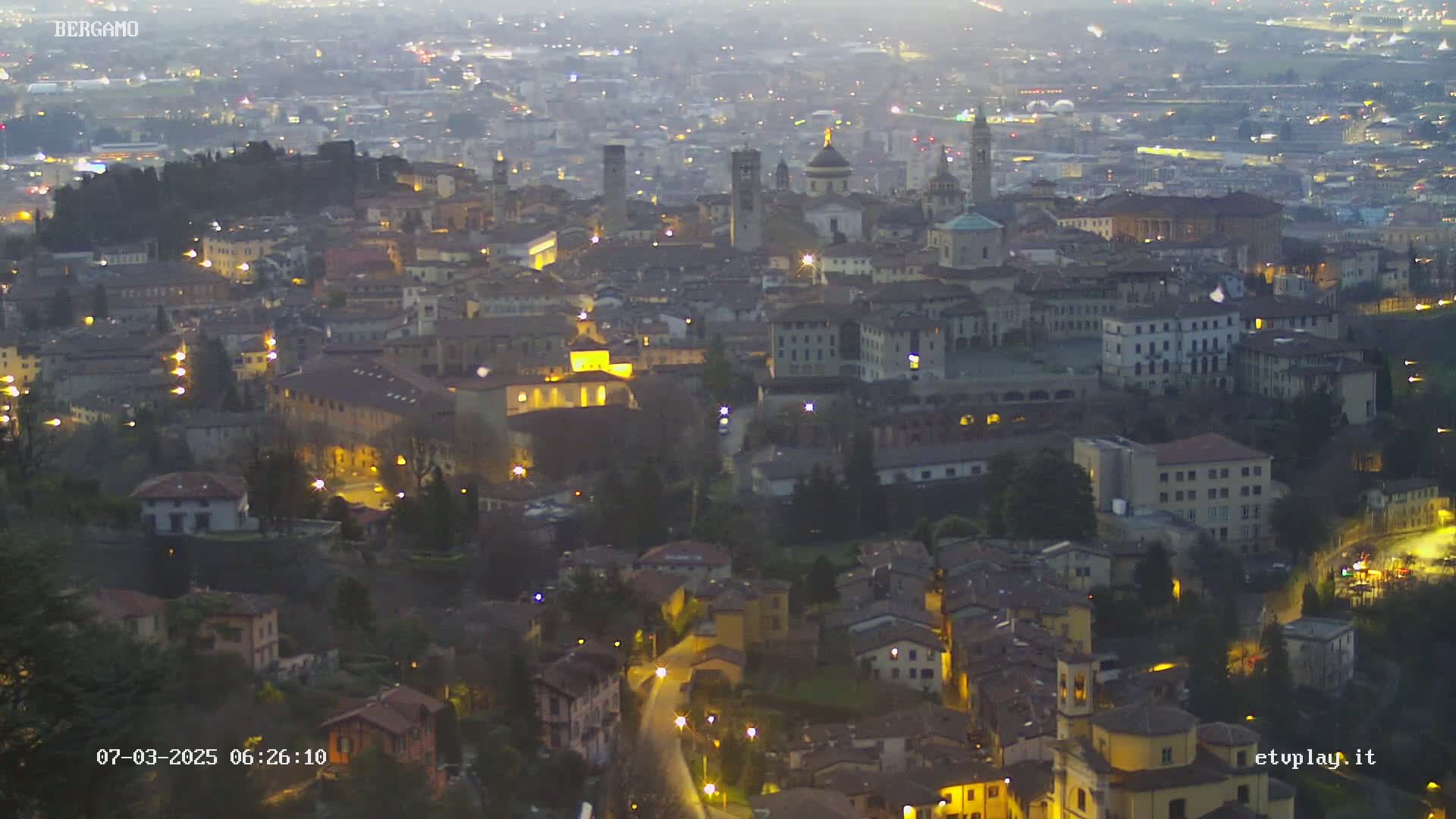 A sprawling city at twilight, illuminated by streetlights, is seen from a high vantage point.