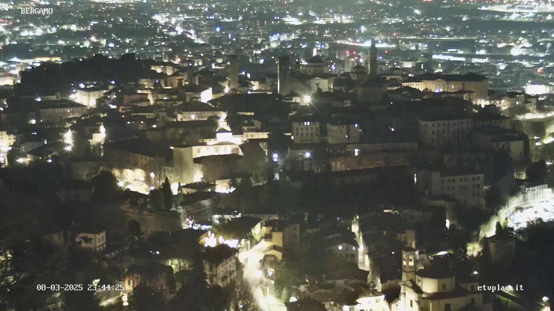 A nighttime aerial view of a city illuminated by streetlights, showing a dense collection of buildings nestled together.