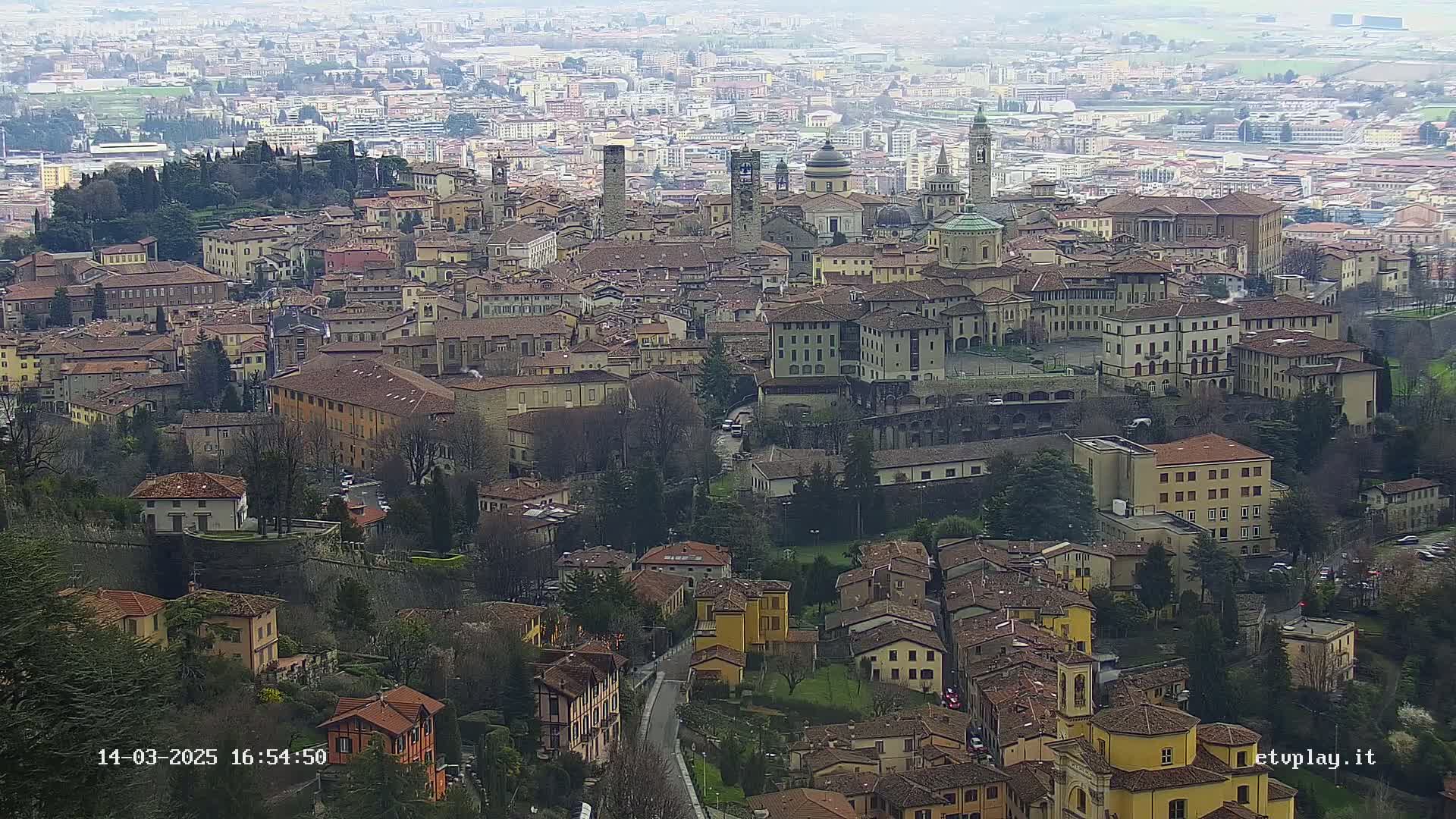An aerial view shows a dense collection of low-rise buildings in a European city on an overcast day.