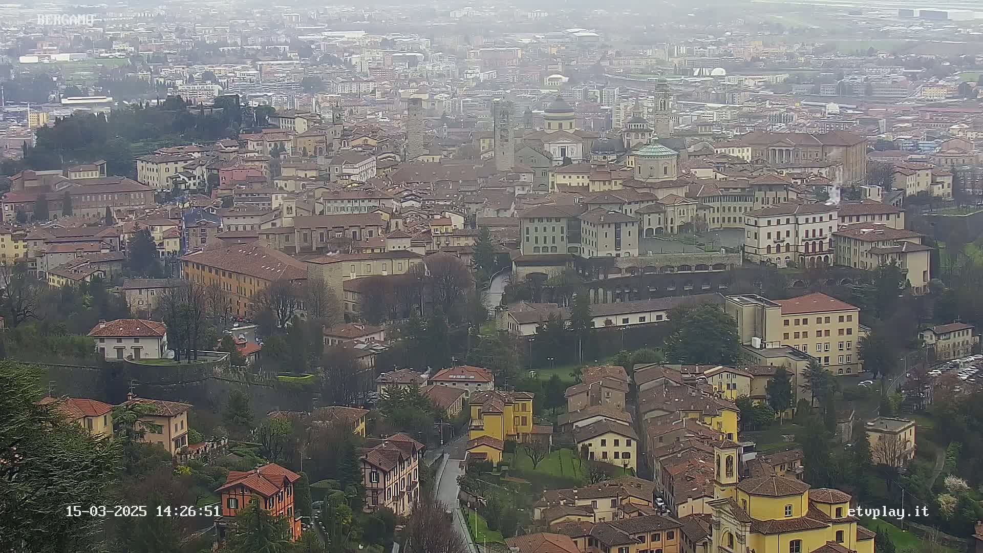 A sprawling city with many tan and brown buildings is viewed from above on an overcast day.