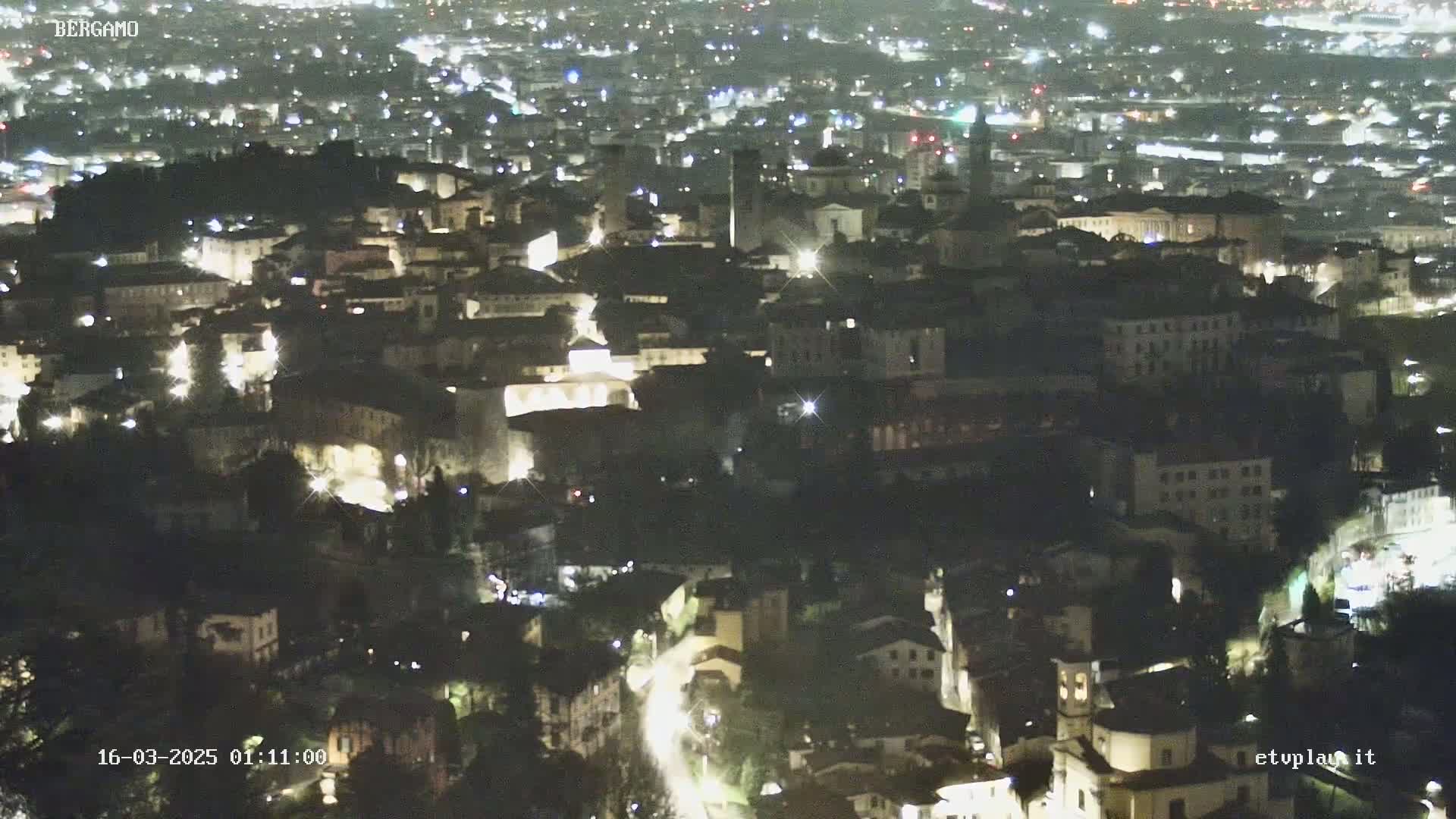 A nighttime aerial view of a city with many buildings illuminated by lights.