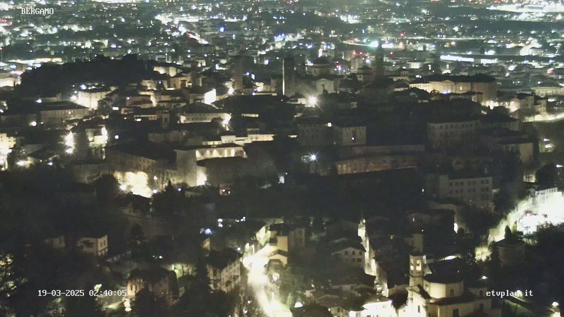 A nighttime, aerial view of a city with numerous buildings illuminated by lights.