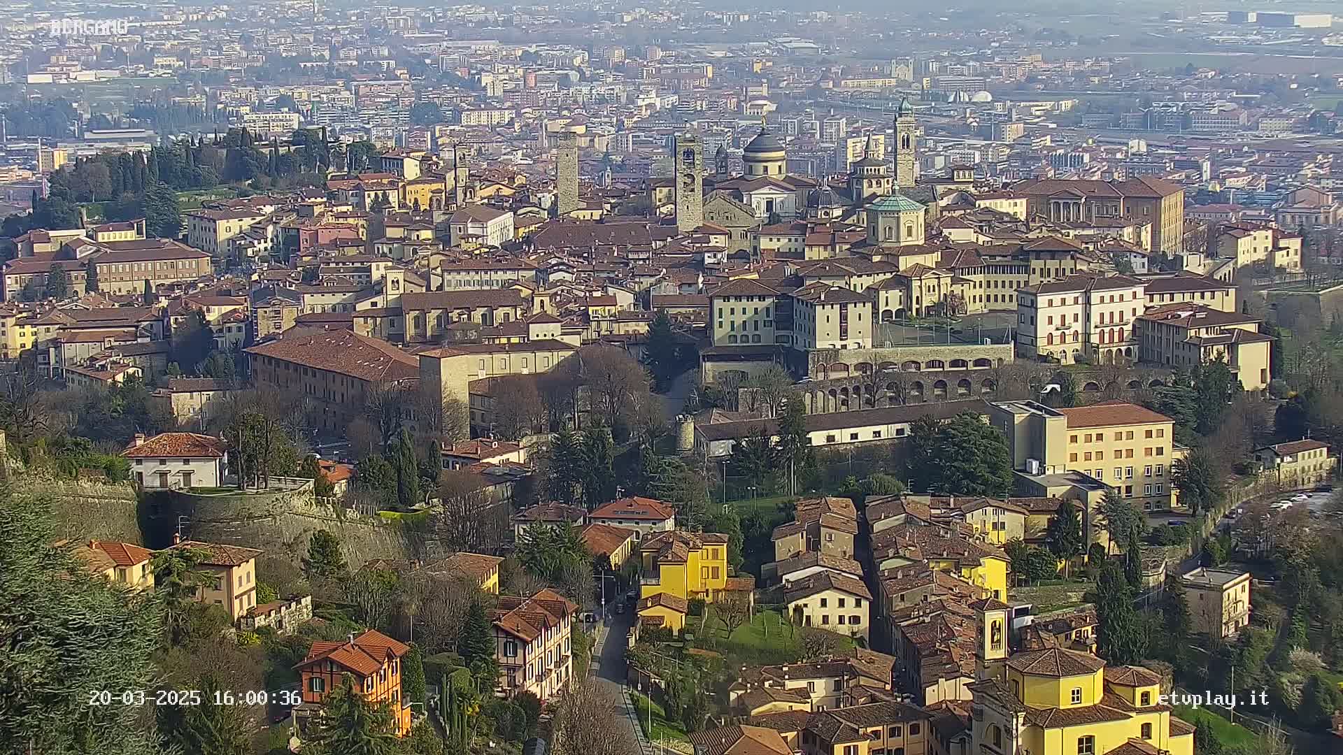 A sprawling city of closely packed, tan and brown buildings nestled within a valley on a hazy day.