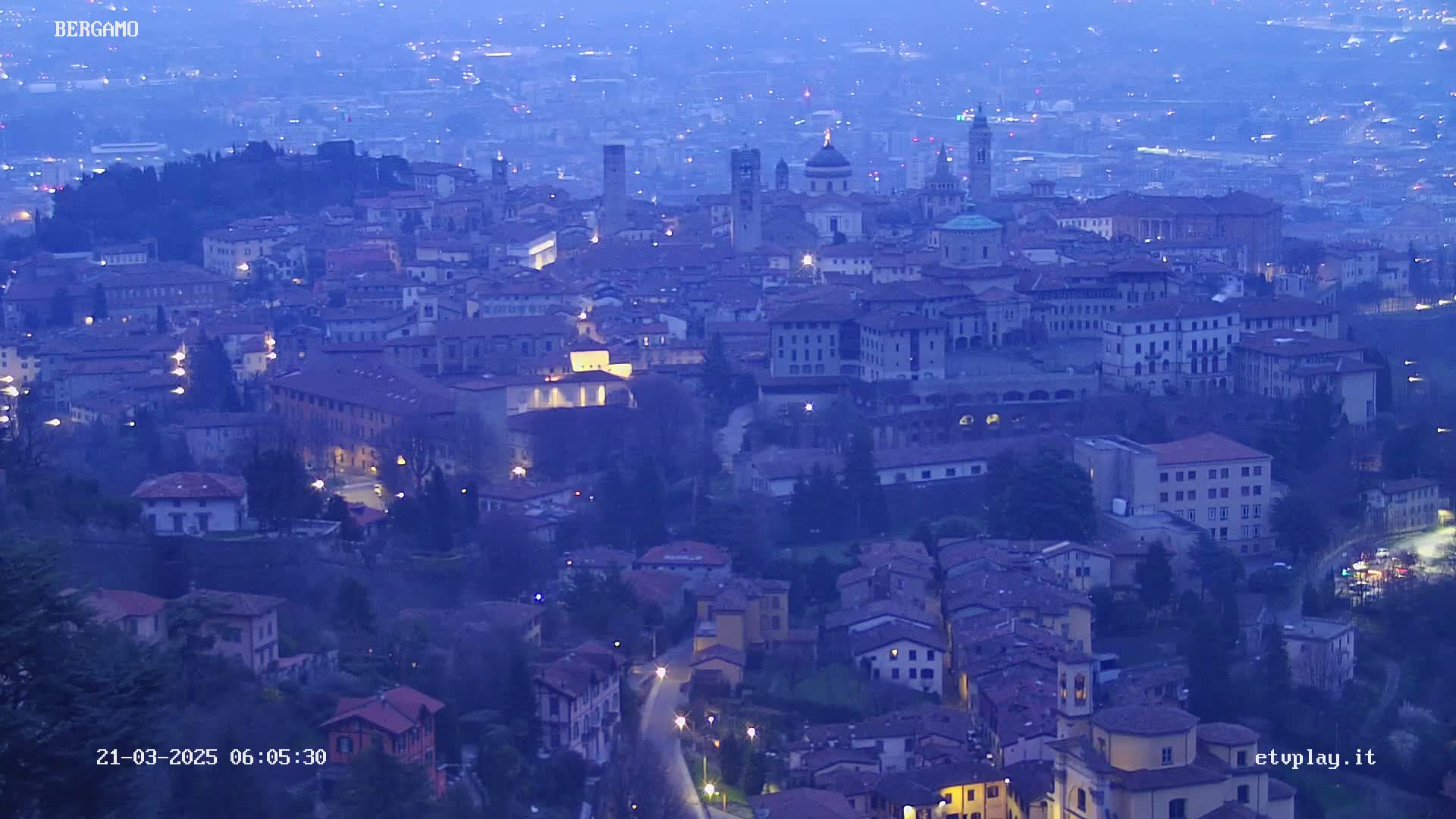 A sprawling city at dusk, illuminated by streetlights, under a hazy sky.