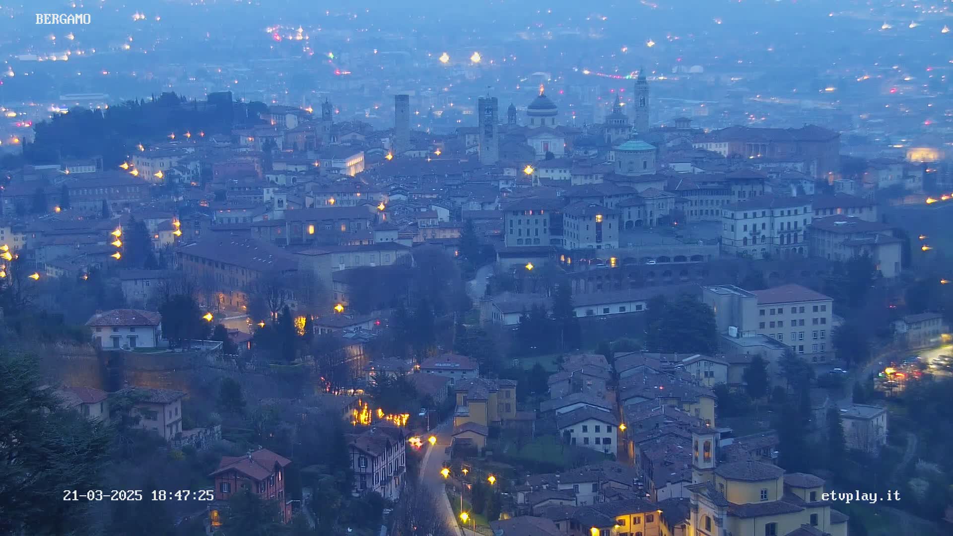 A sprawling city at twilight, illuminated by streetlights, under a dusky blue sky.