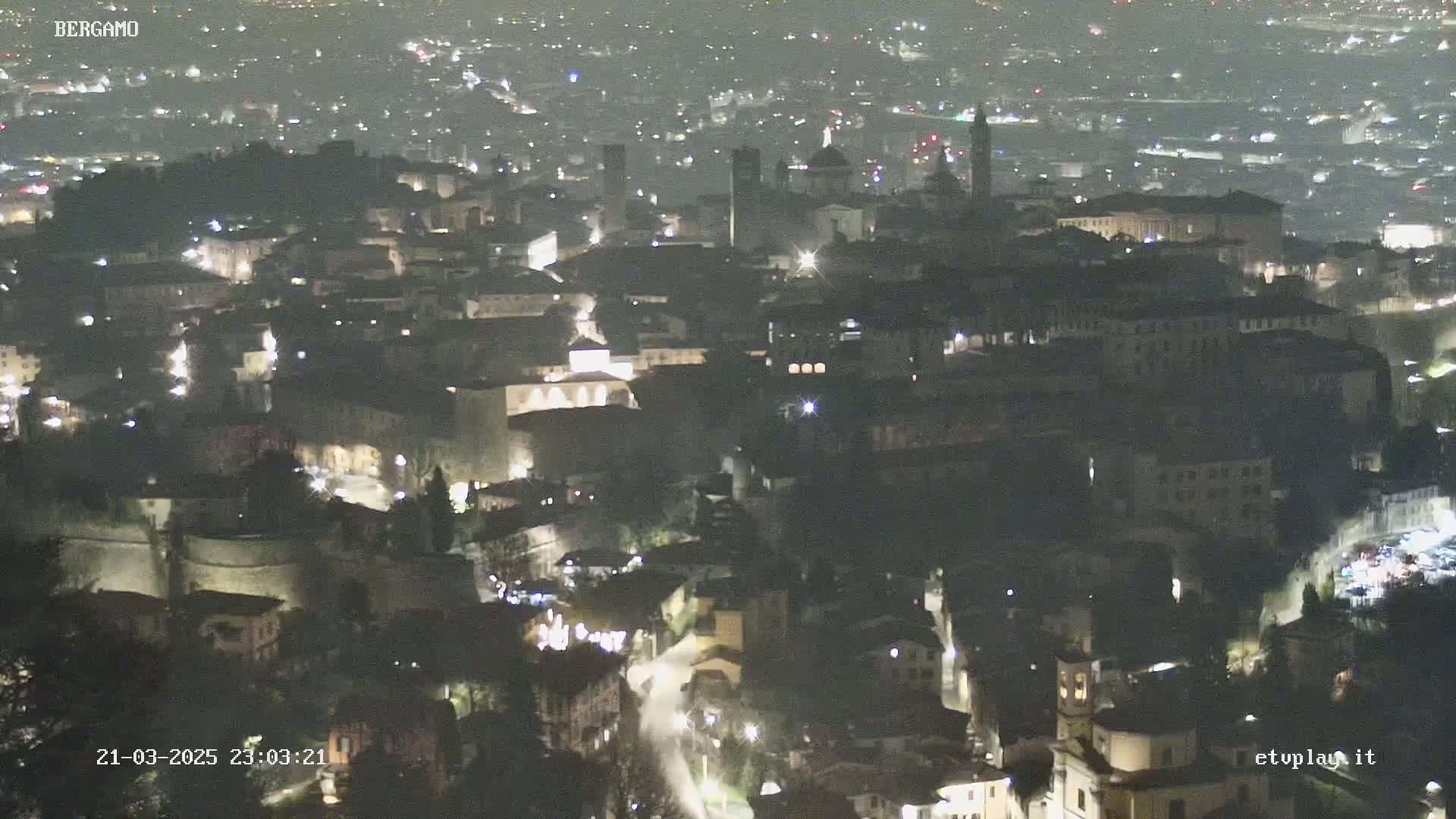 A nighttime aerial view of a city shows many buildings illuminated with lights under a clear, dark sky.