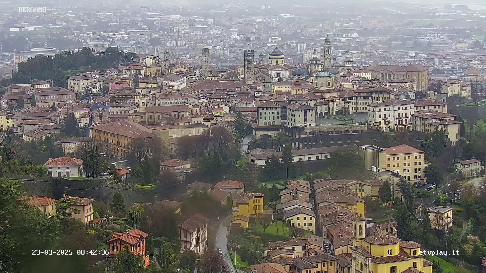 A sprawling city with numerous buildings of varying heights and architectural styles is viewed from above on an overcast day.