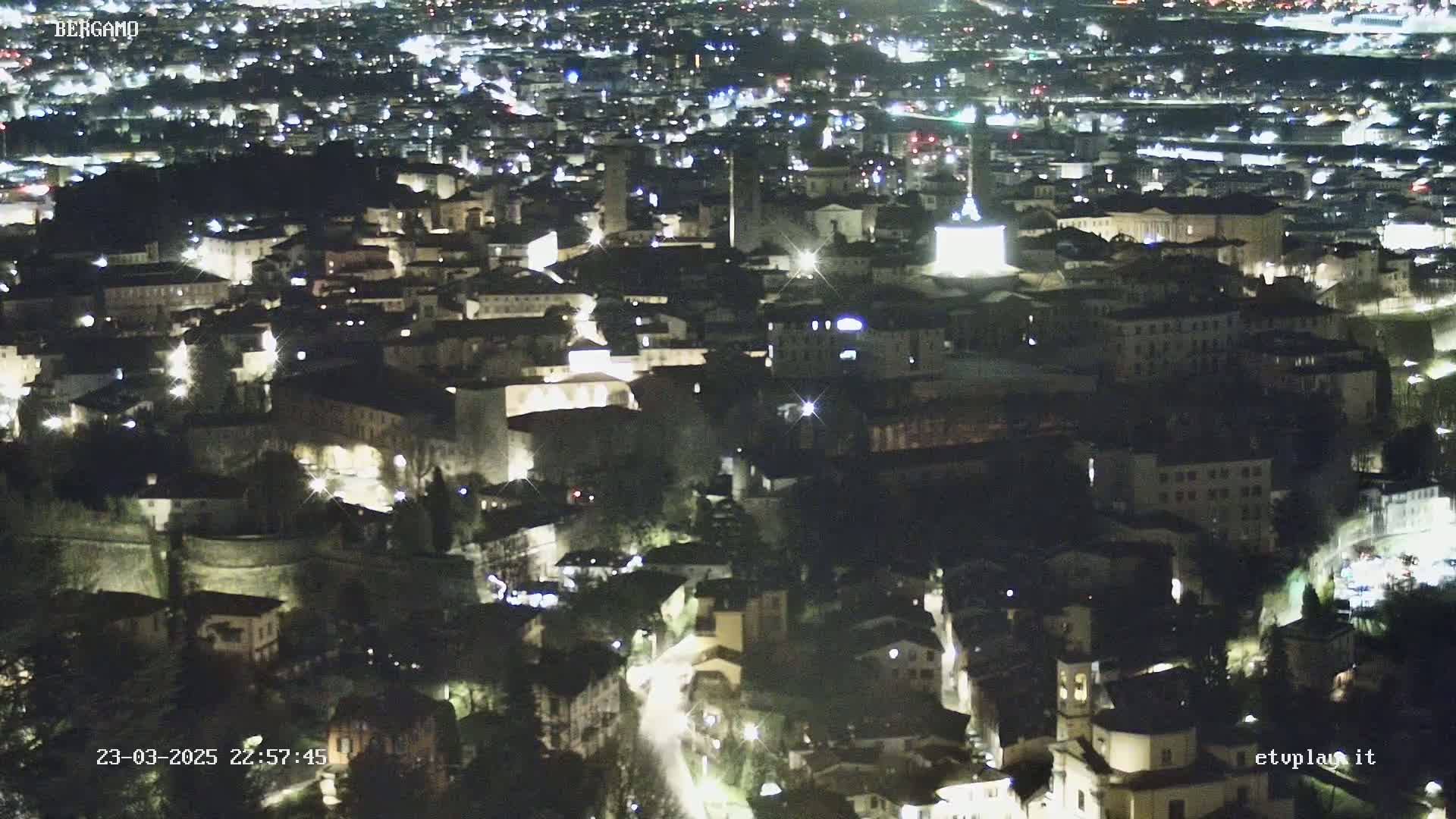 A nighttime aerial view of a city, showing many buildings illuminated with lights.