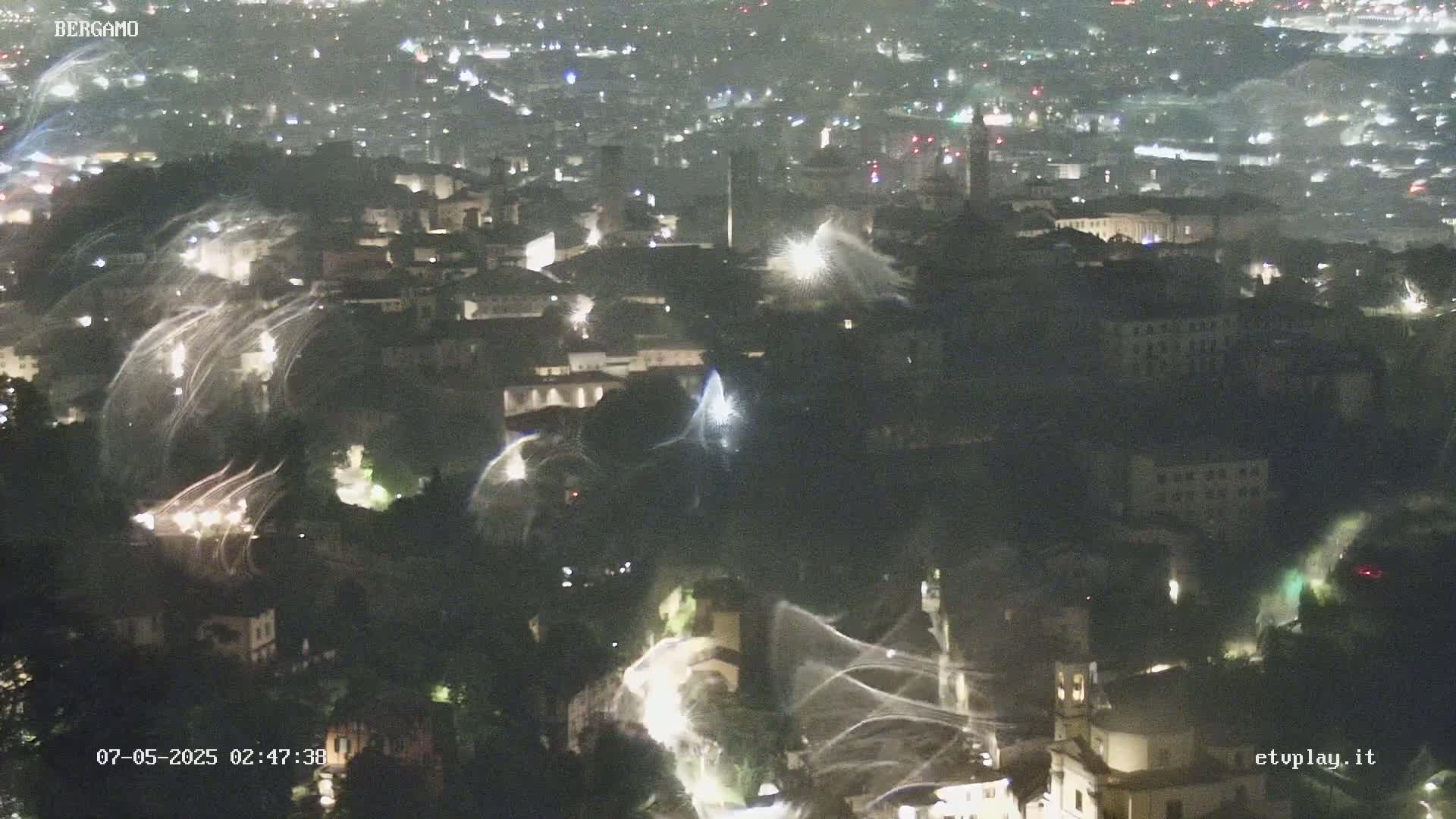A nighttime, aerial view of a city with streaks of light possibly caused by rain or wind across the illuminated buildings and streets.