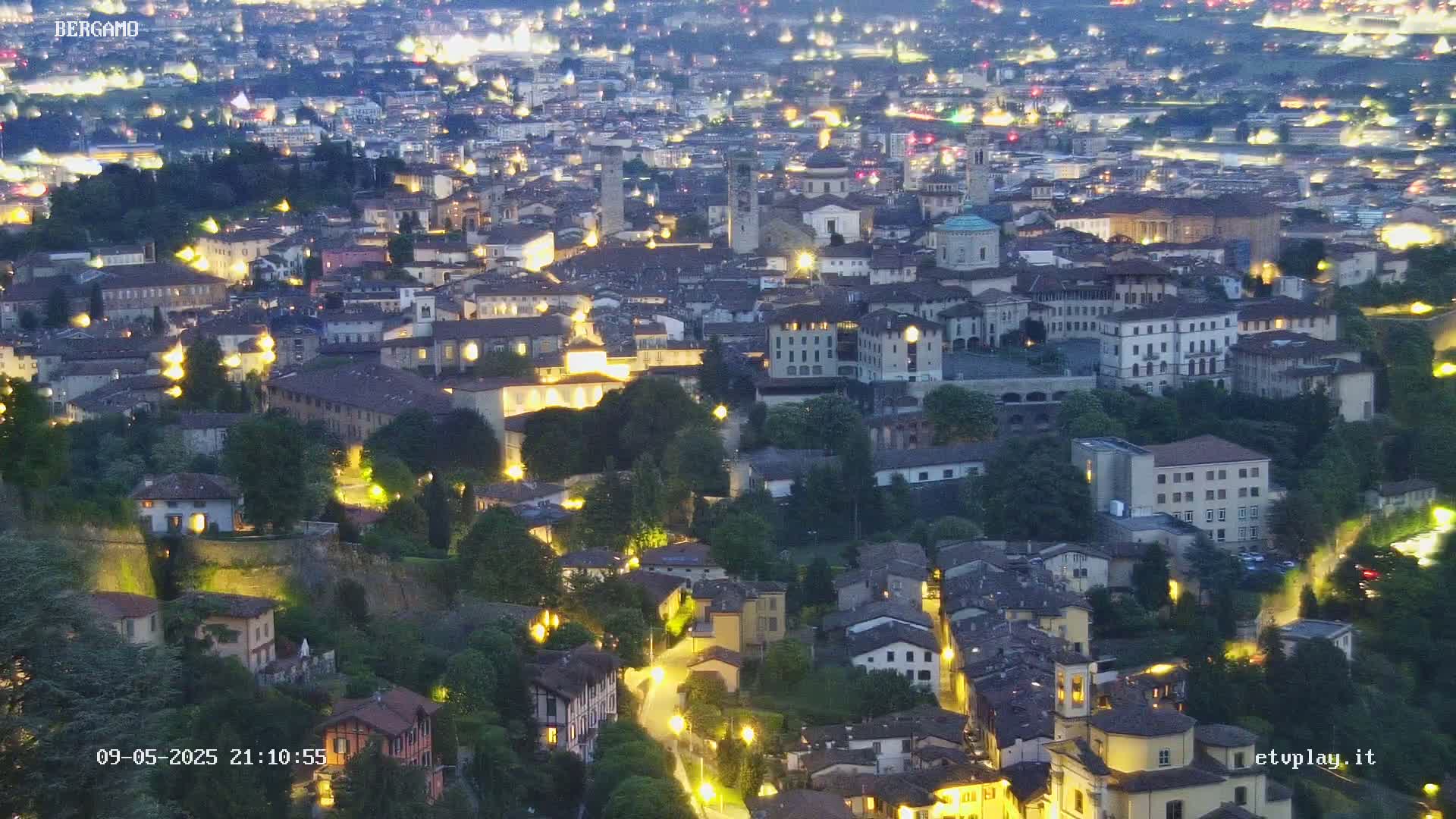 A nighttime aerial view of a city nestled in a valley, illuminated by streetlights and the warm glow of buildings.