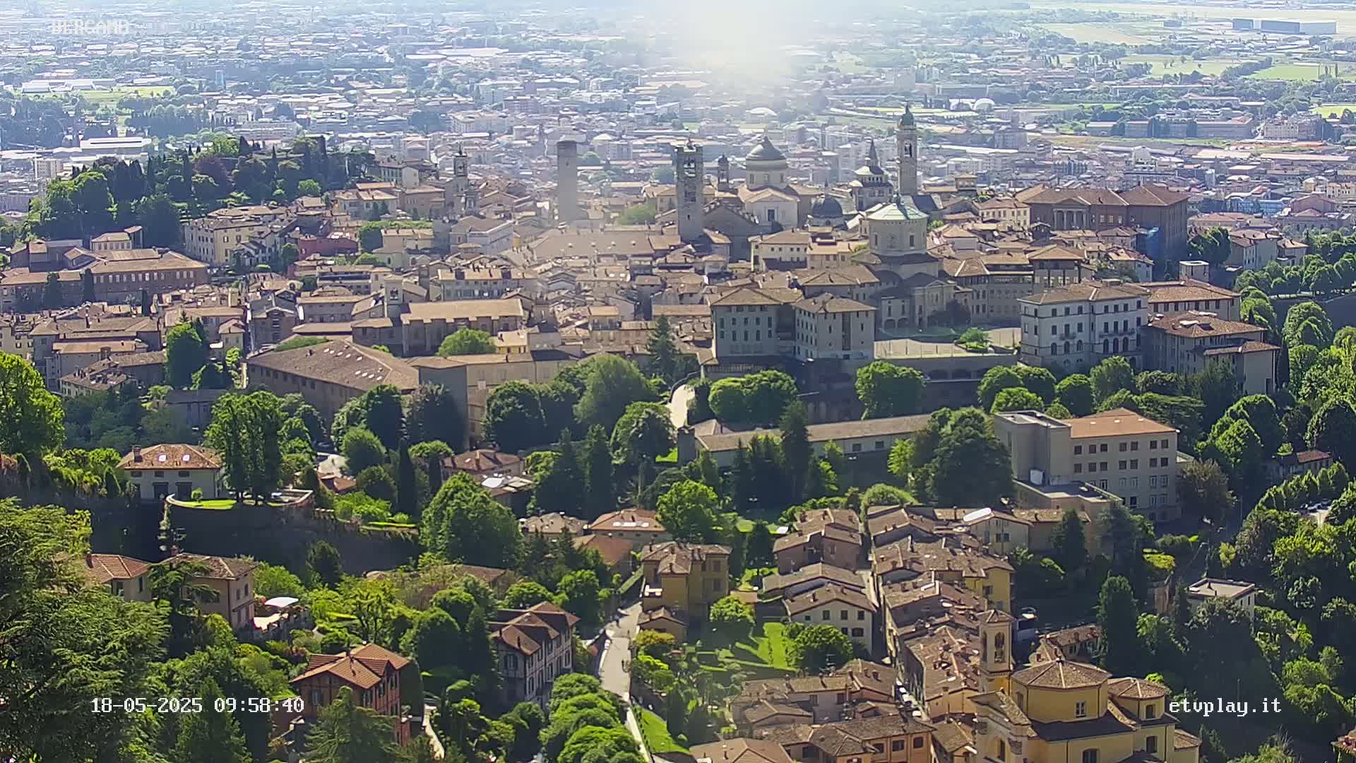 A sprawling city with many tan buildings, surrounded by lush green trees, on a sunny day.