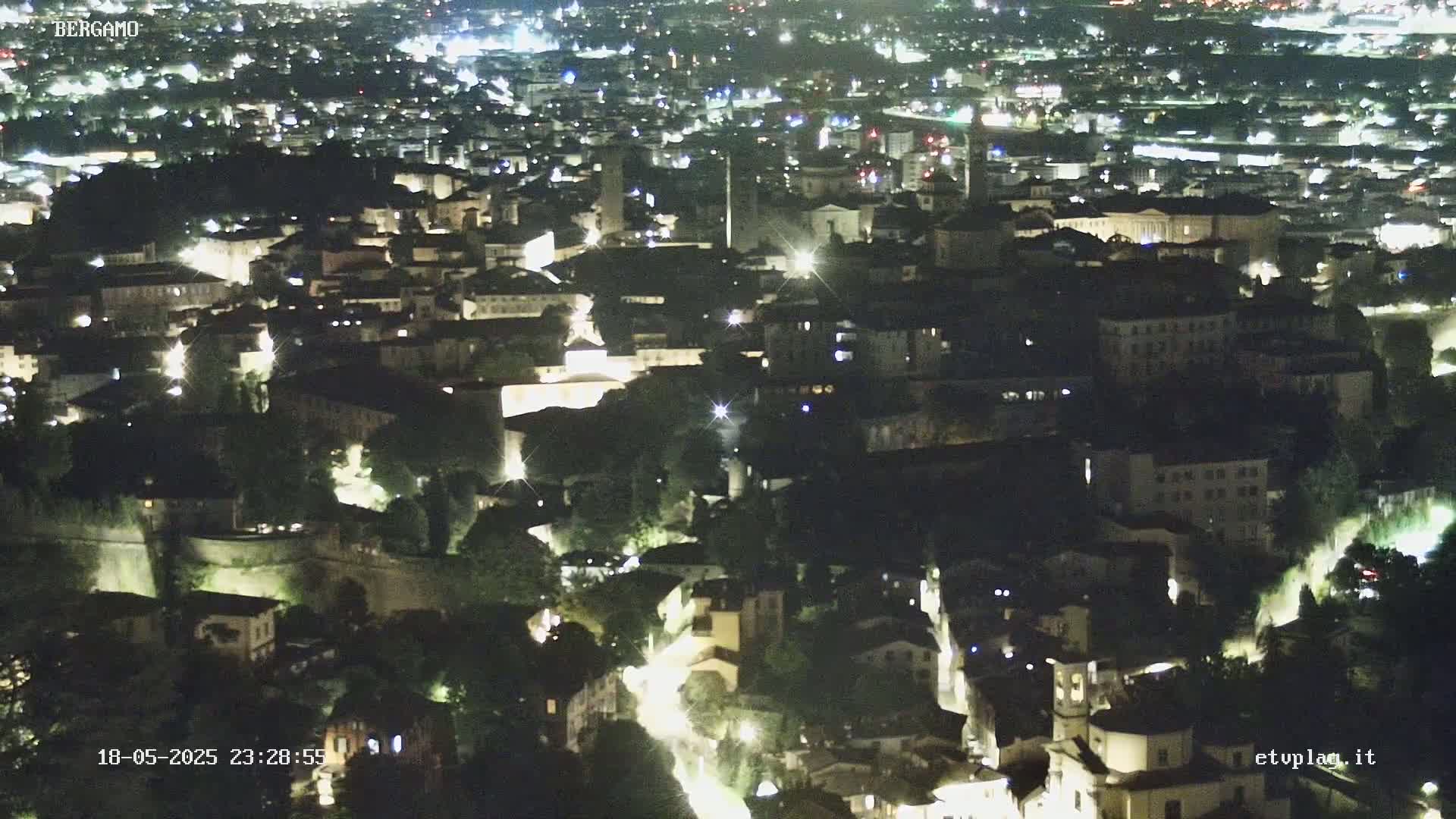 A nighttime aerial view of a city with illuminated buildings and streets, nestled among dark trees.