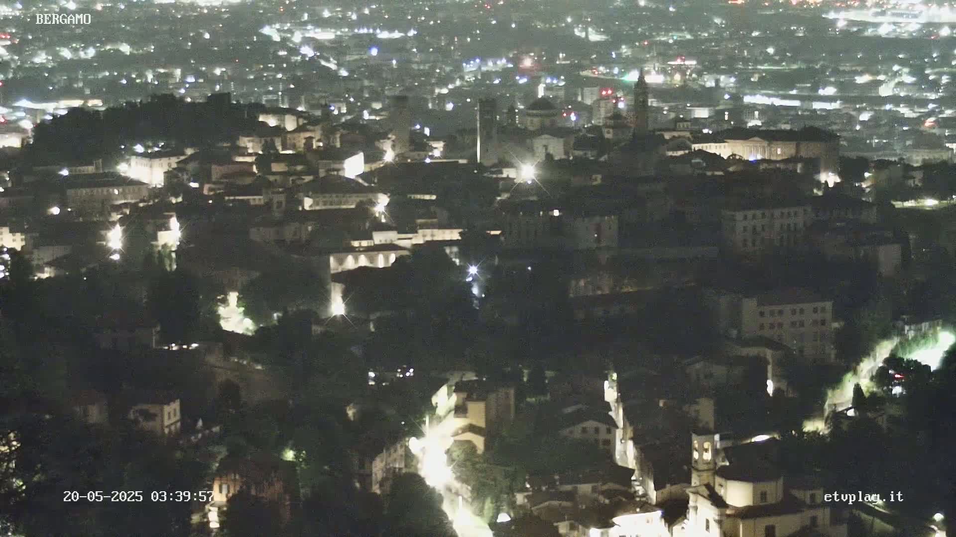 A nighttime aerial view shows a city illuminated by streetlights, with a sprawling landscape of buildings extending into the distance.