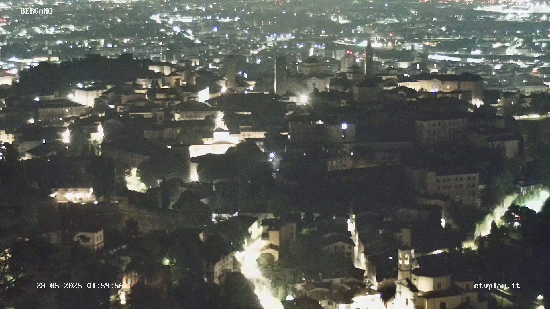 A nighttime, aerial view of a city with numerous illuminated buildings and streets.