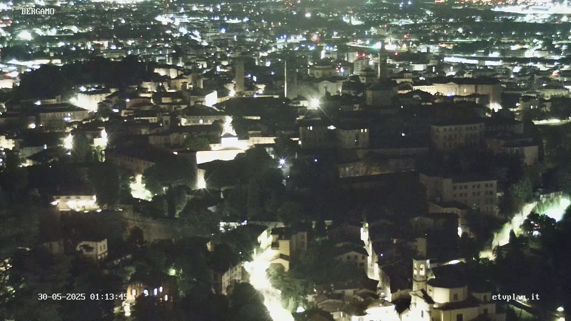 A nighttime aerial view of a city with illuminated buildings and streets nestled among dark trees.