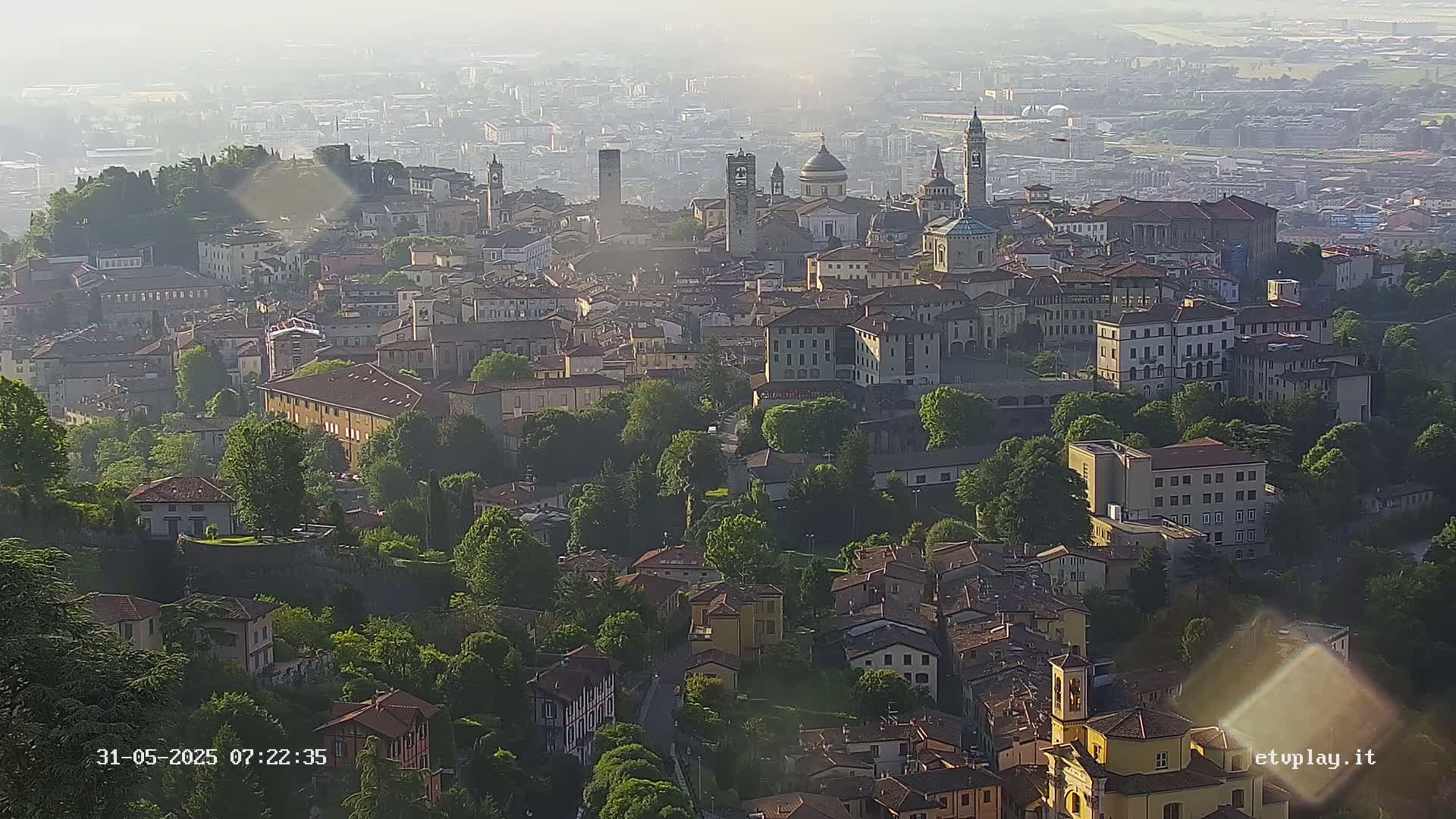 A hazy, high-angle view shows a city nestled among green hills and trees.