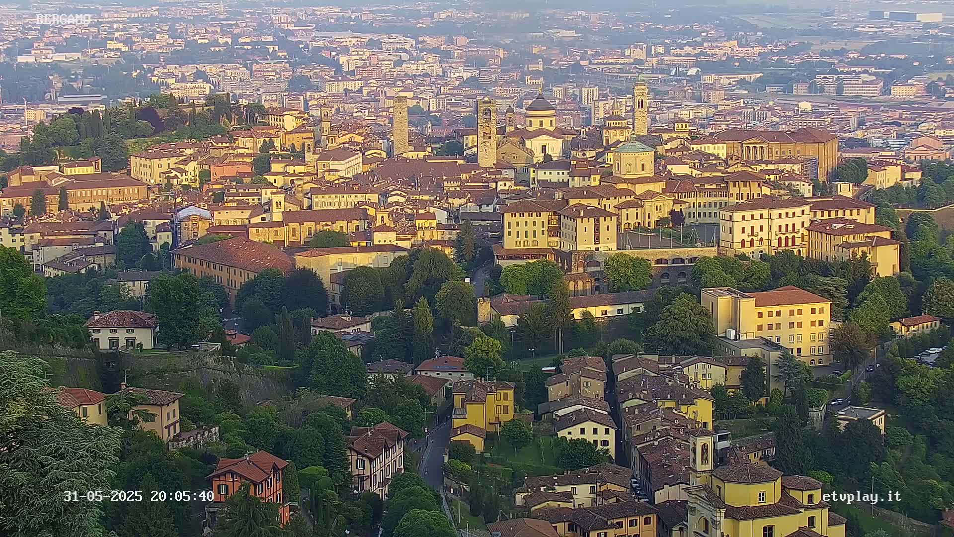 A sprawling city with numerous buildings of varying heights and architectural styles, bathed in the golden light of late afternoon or early evening.