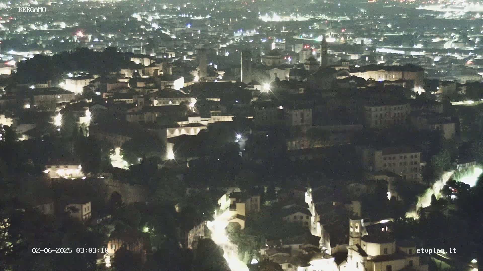 A nighttime aerial view shows a city with many buildings illuminated by lights.