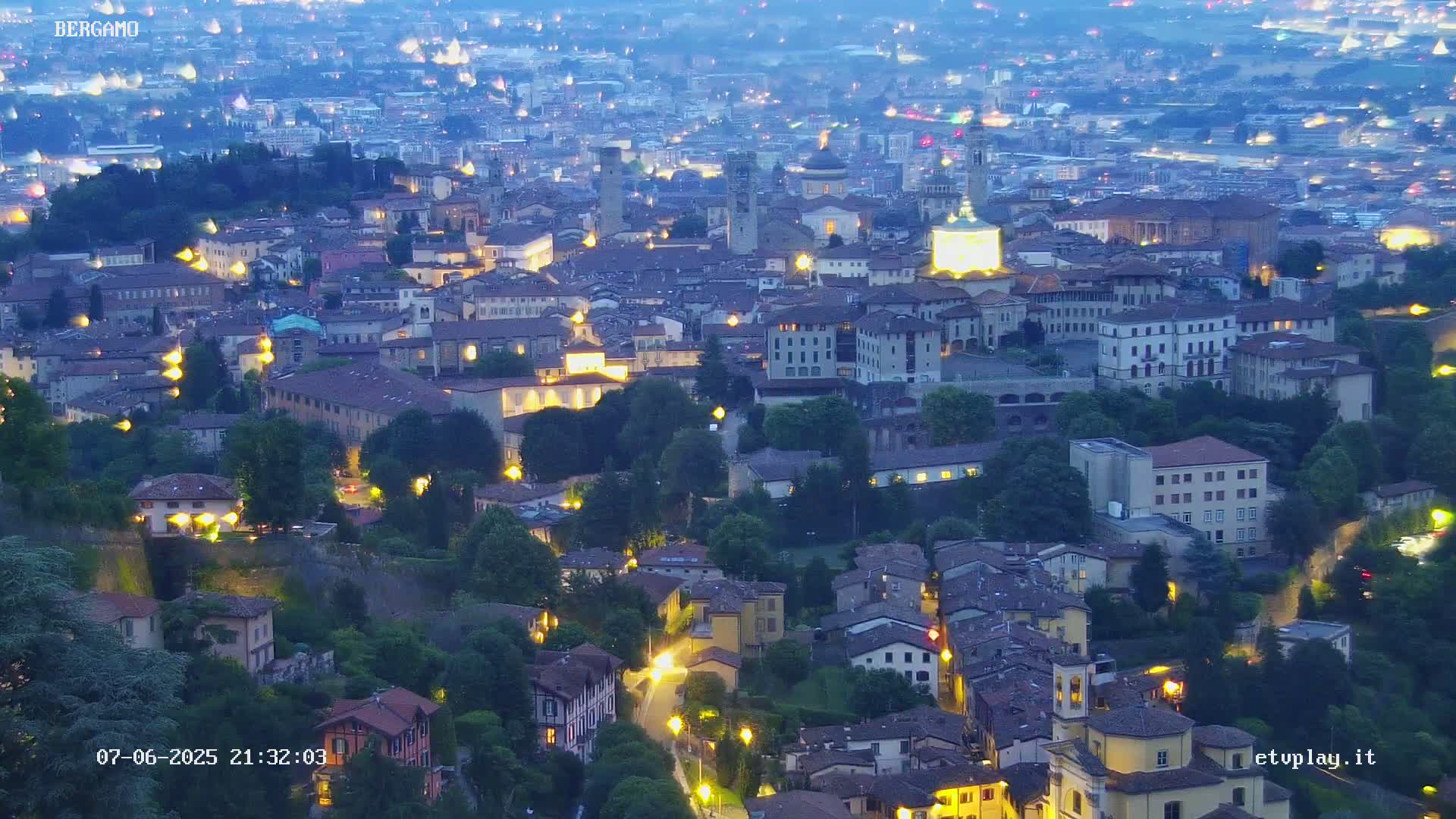 A nighttime aerial view of a city nestled in a valley, illuminated by streetlights and the glow of buildings.