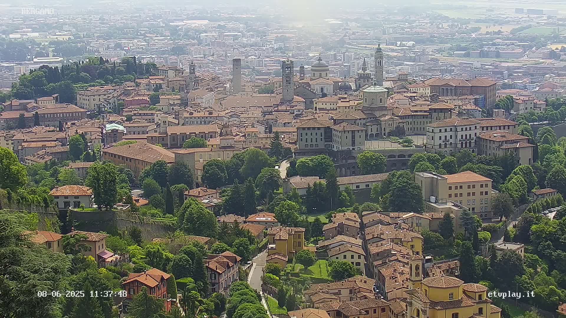 A hazy view of a dense, historic European city nestled within a lush, green landscape.
