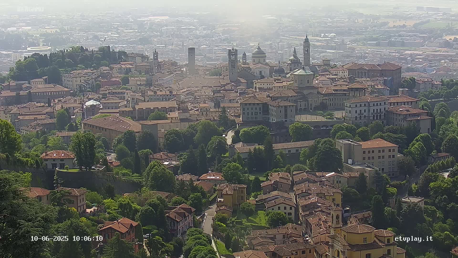 A hazy, elevated view of a dense European city with numerous buildings, churches, and green spaces.