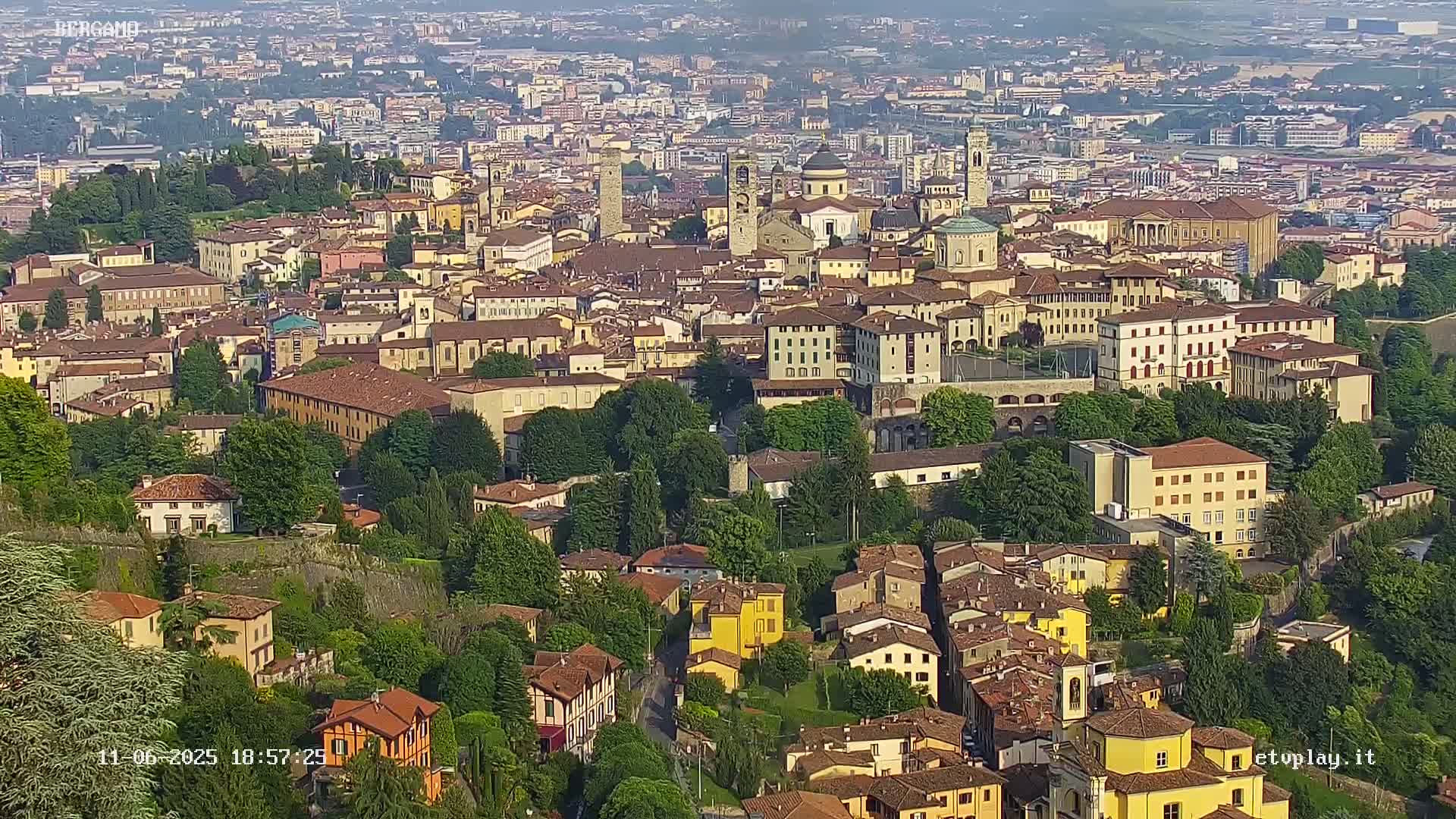 A sprawling city with numerous buildings of varying heights and architectural styles, nestled among lush green trees and hills under a hazy sky.