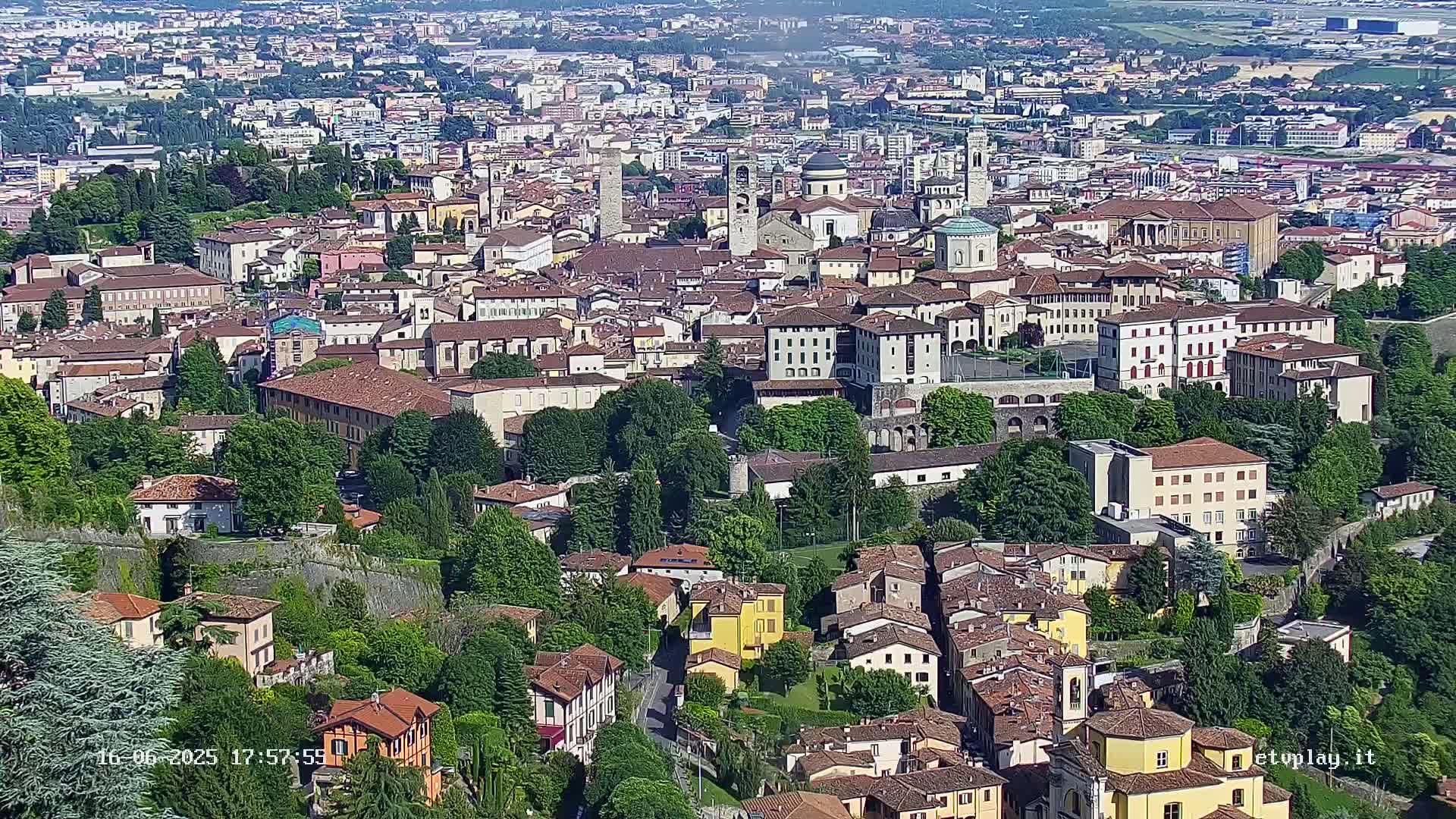 A sprawling cityscape of closely packed buildings and green spaces, viewed from above on a sunny day.