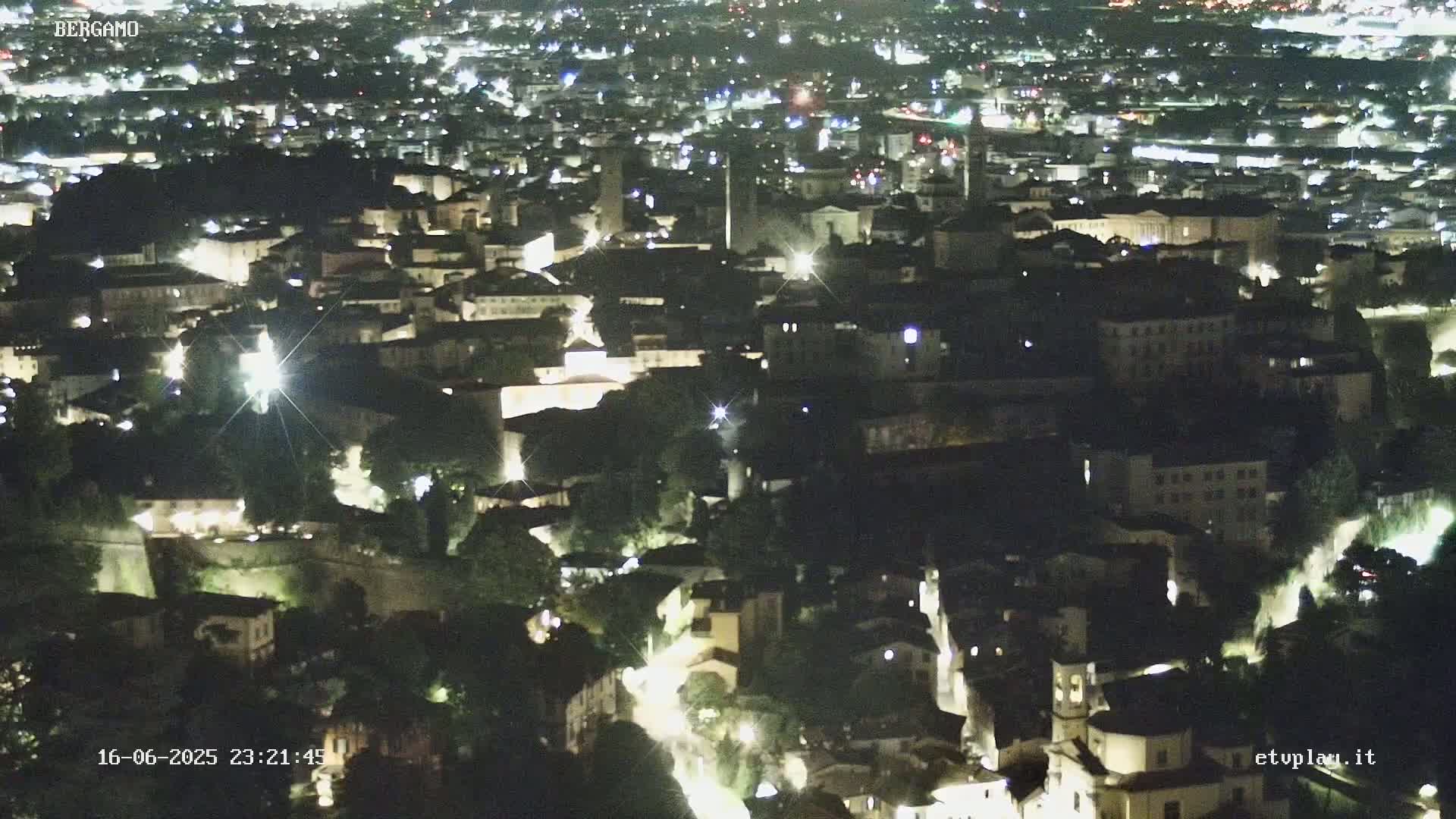 A nighttime aerial view of a city with illuminated buildings and streets nestled among dark trees.
