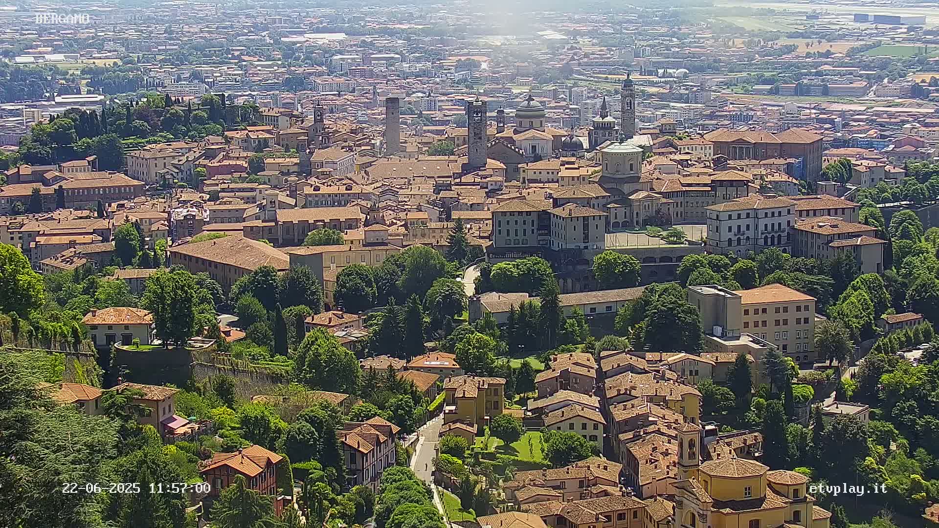 A sprawling city of terracotta-roofed buildings nestled amongst lush green trees on a sunny day.