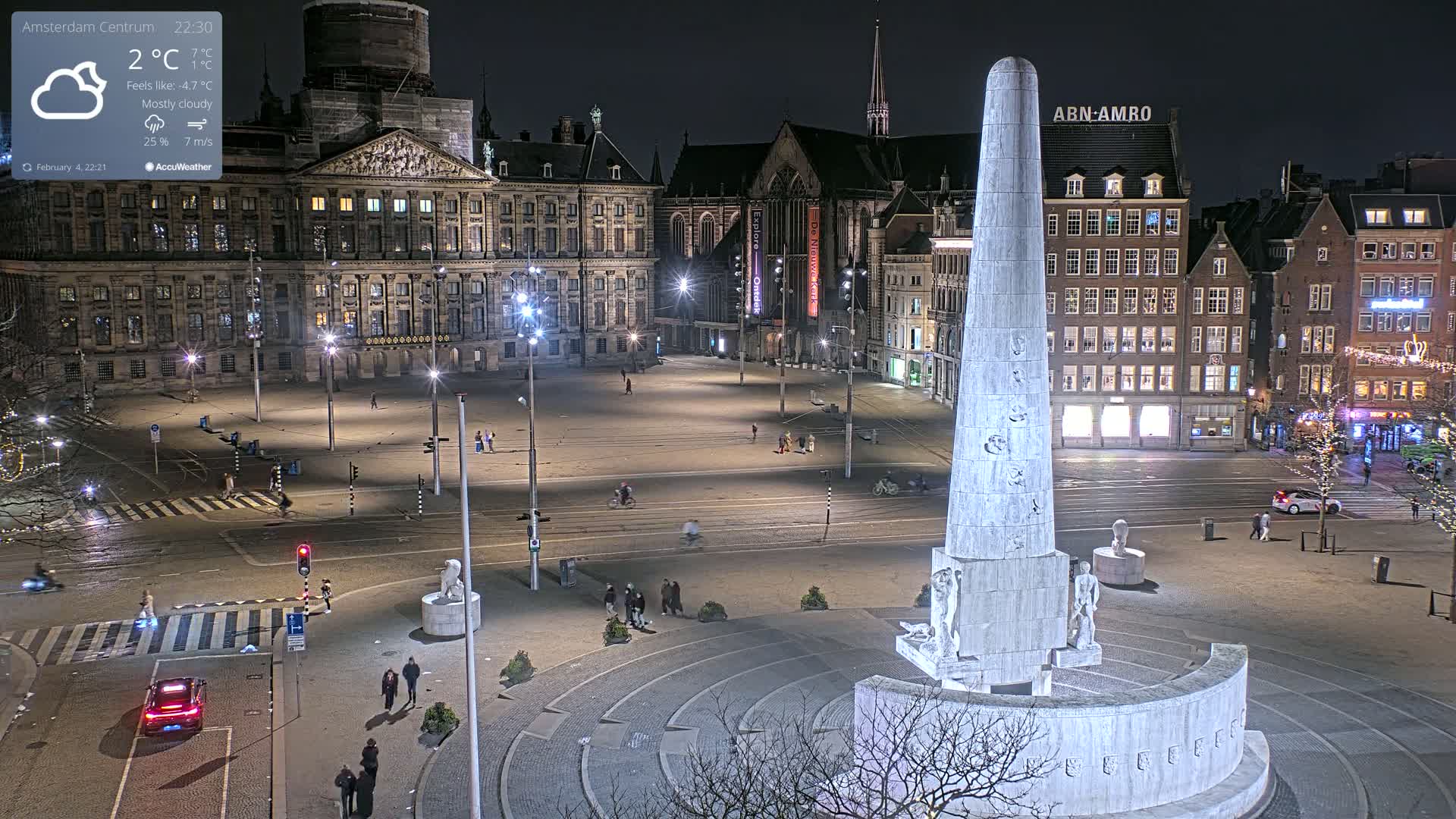 A mostly cloudy night scene shows a large, empty square in a city with a tall monument at the bottom center, surrounded by buildings and streetlights.
